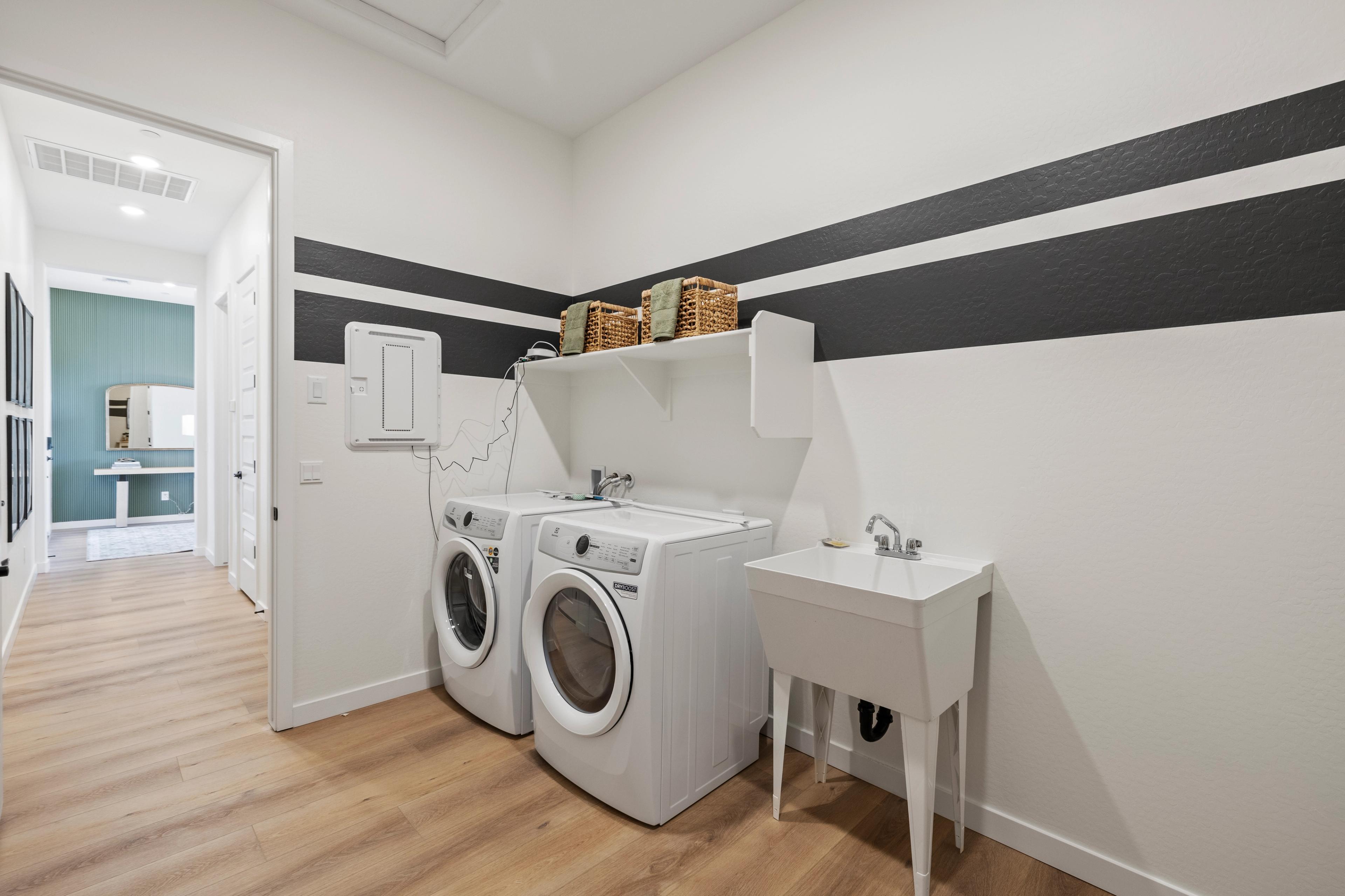 Spacious laundry room at Hidden Hills in Prescott AZ with white washers, utility sink, black striped walls, and hardwood floors