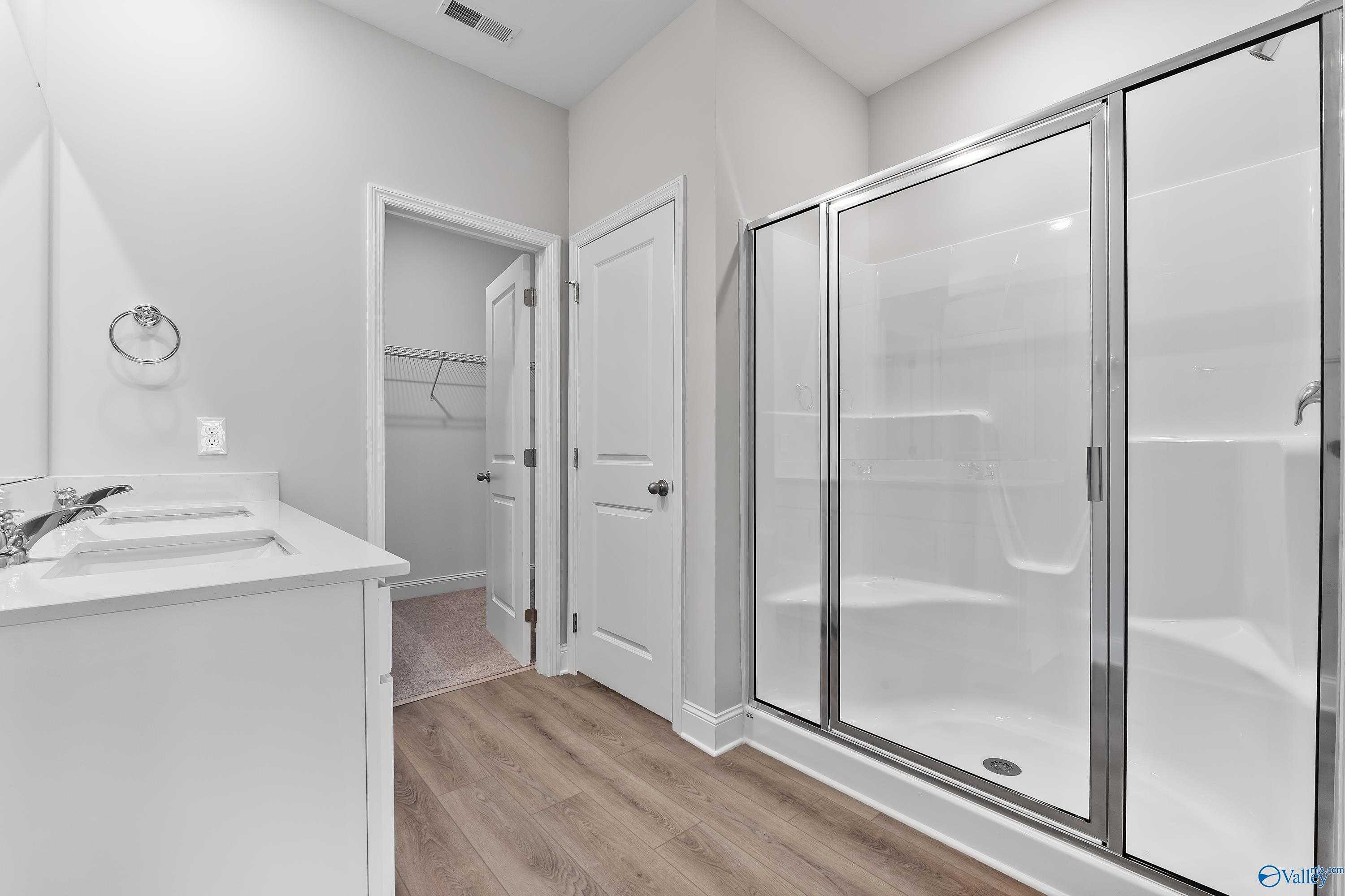 Modern master bathroom featuring white double vanity, frameless glass shower, and adjacent walk-in closet in Davidson Homes The Franklin C, Toney, Alabama