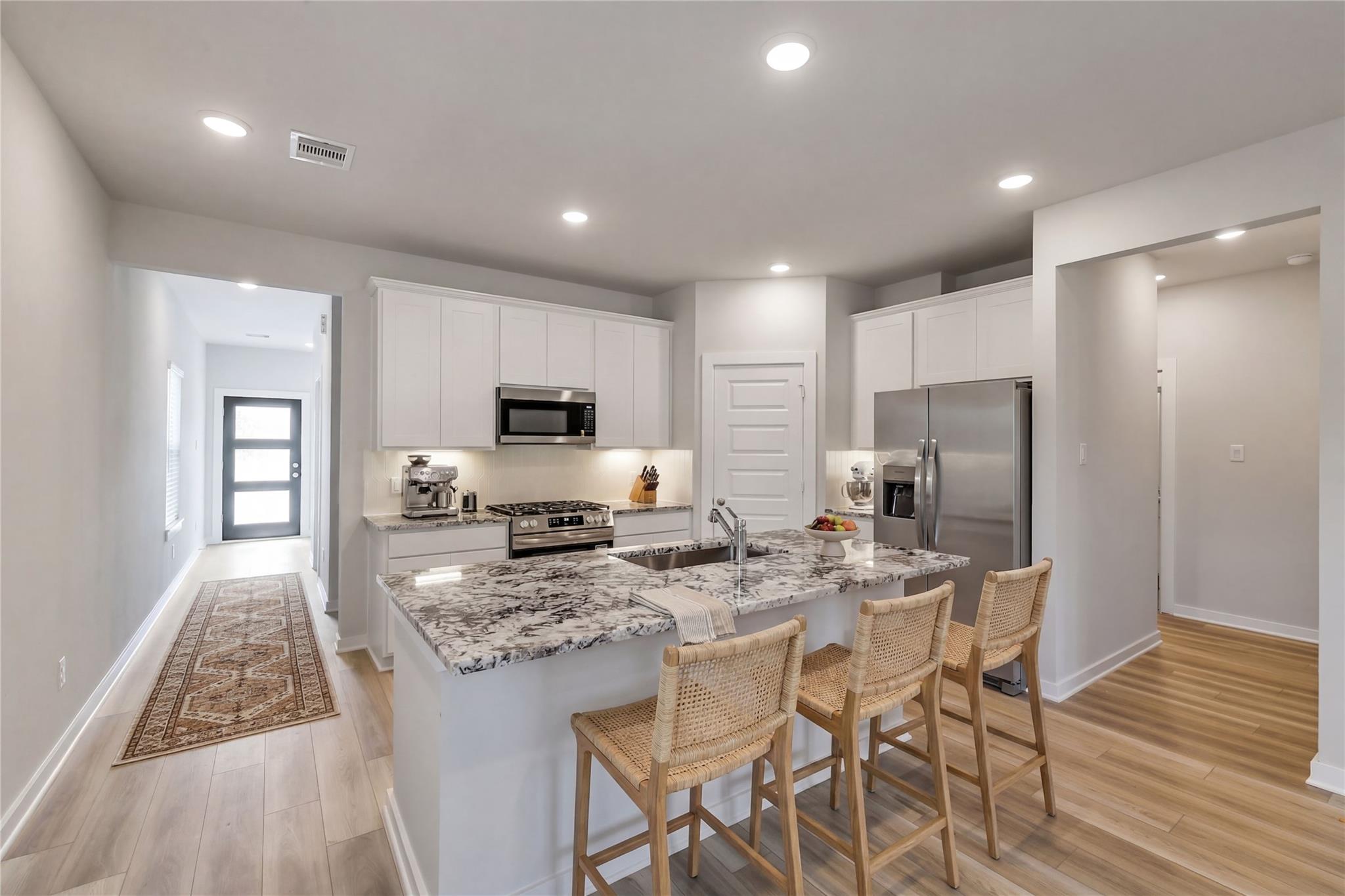 Modern open-concept kitchen with white cabinets, granite island, stainless appliances in 5-bed San Marcos E home, Conroe TX