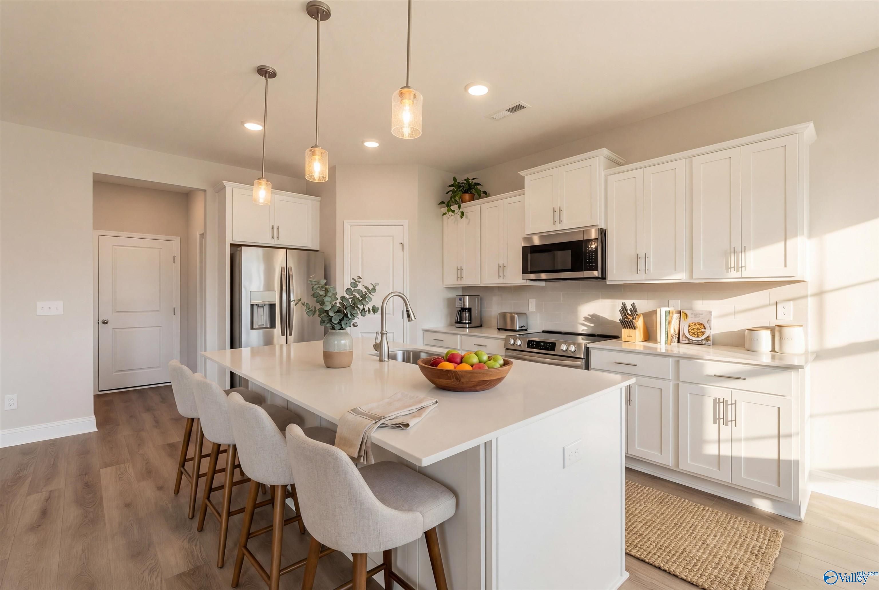 Modern white kitchen with stainless appliances, large island, and pendant lights in Davidson Homes The Montgomery B, Toney, AL