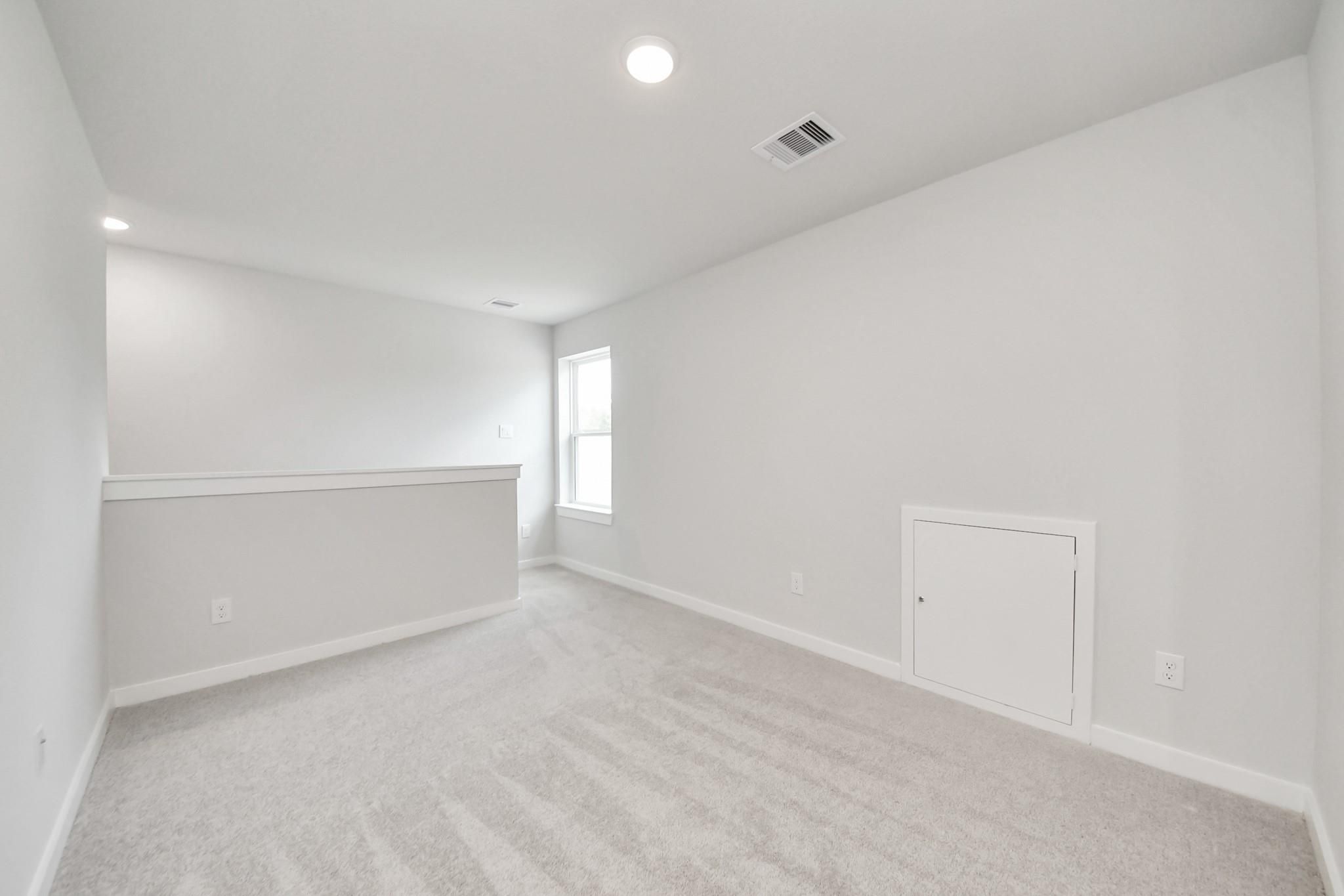 Bright carpeted loft area with attic access in The Blanco E floor plan at Caney Creek Place, Conroe, Texas.