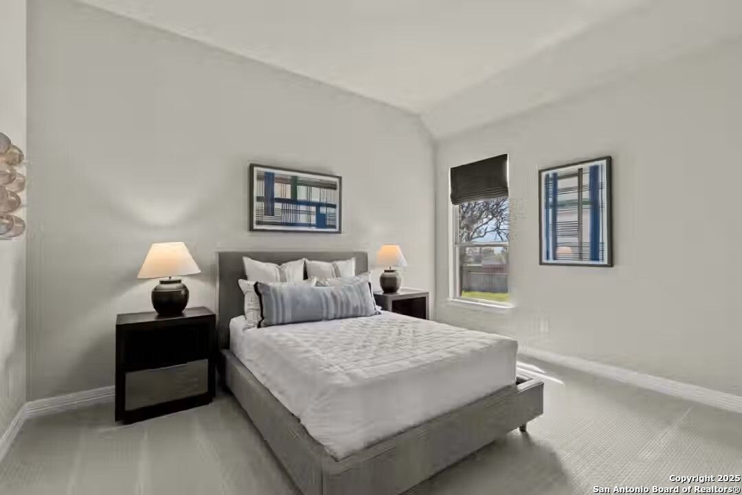 Serene guest bedroom with gray upholstered bed, neutral walls, abstract art, and tree-view window in The Summerlin B, Castroville, Texas