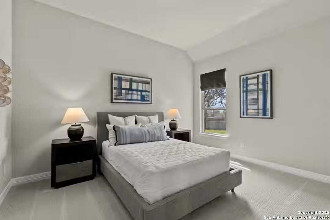 Serene guest bedroom with gray upholstered bed, neutral walls, abstract art, and tree-view window in The Summerlin B, Castroville, Texas