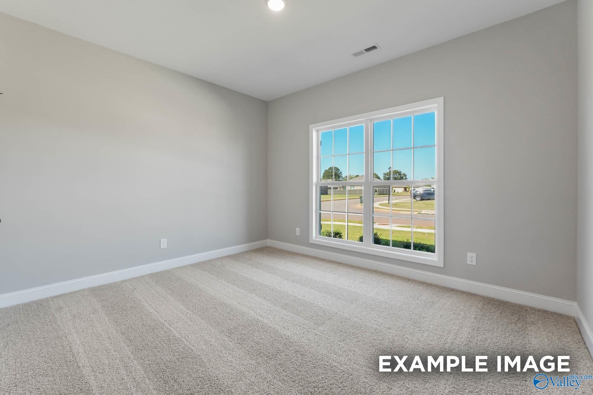 Bright empty bedroom with gray walls, carpet flooring, and large window view of Ricketts Farm neighborhood in Davidson Homes The Daphne C, Athens, Alabama