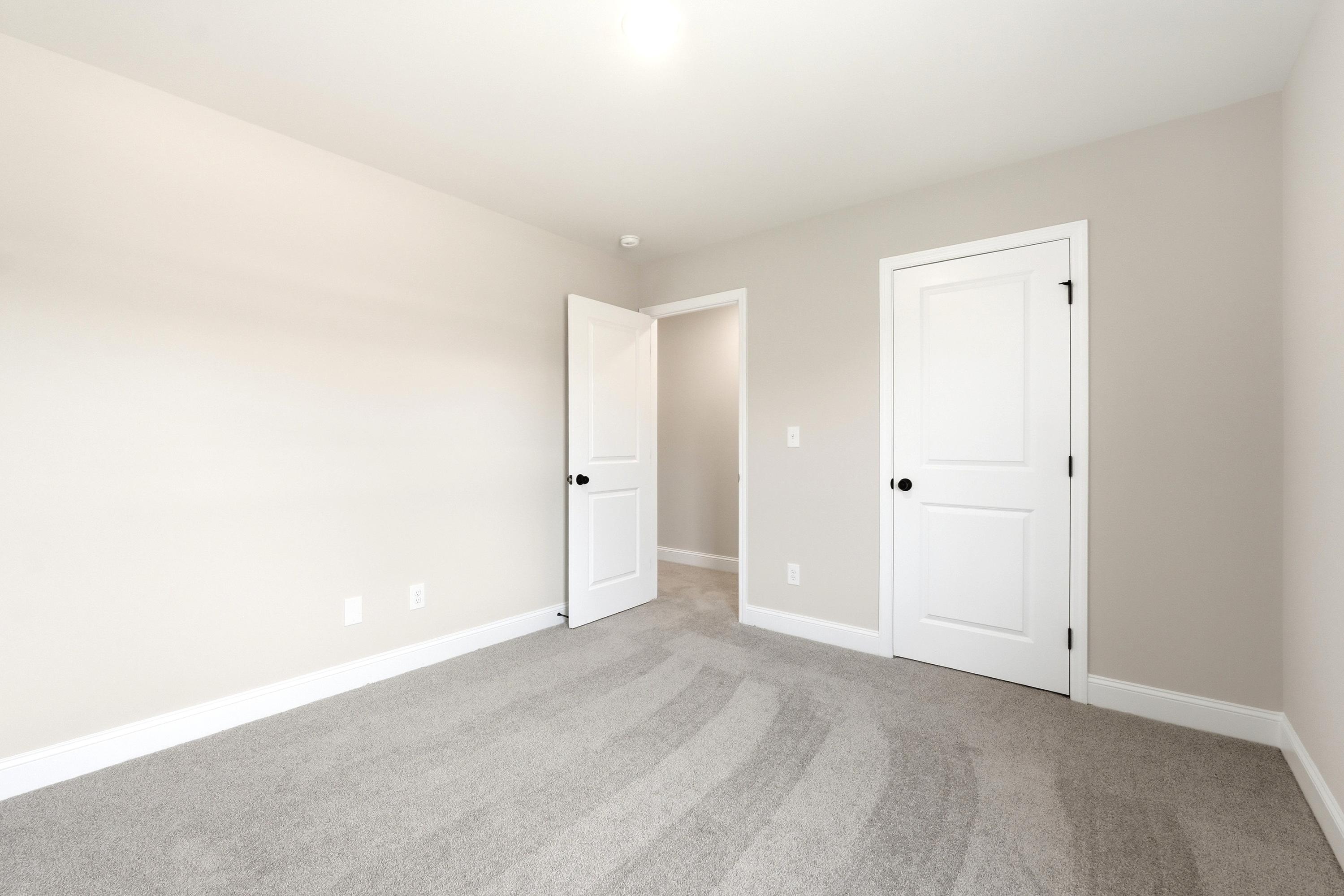 Spacious secondary bedroom in The Russell A featuring neutral paint, plush carpeting, and a walk-in closet.