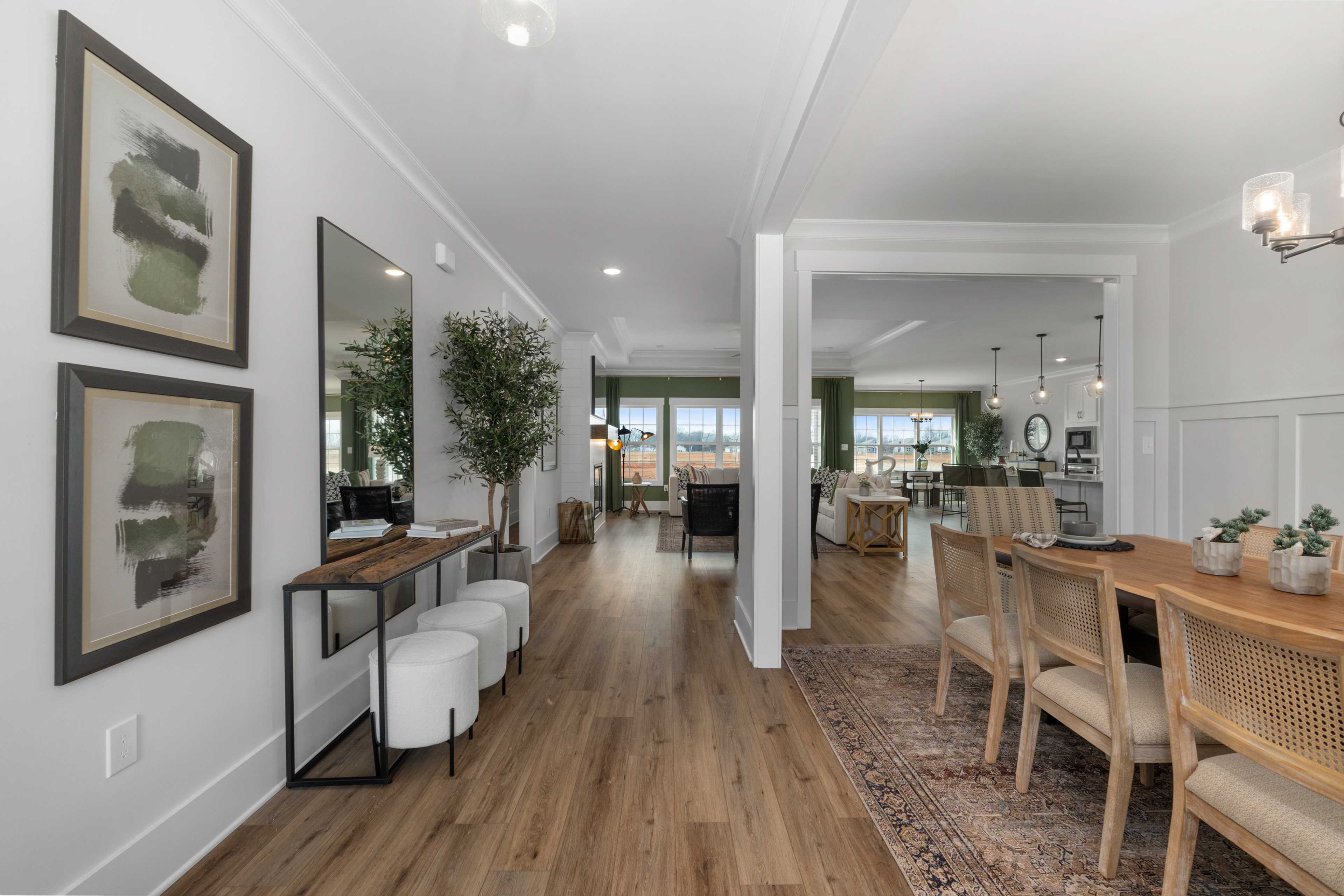 Spacious hallway and dining area at Briercreek in Meridianville, Alabama with hardwood floors, modern artwork, and rattan chairs