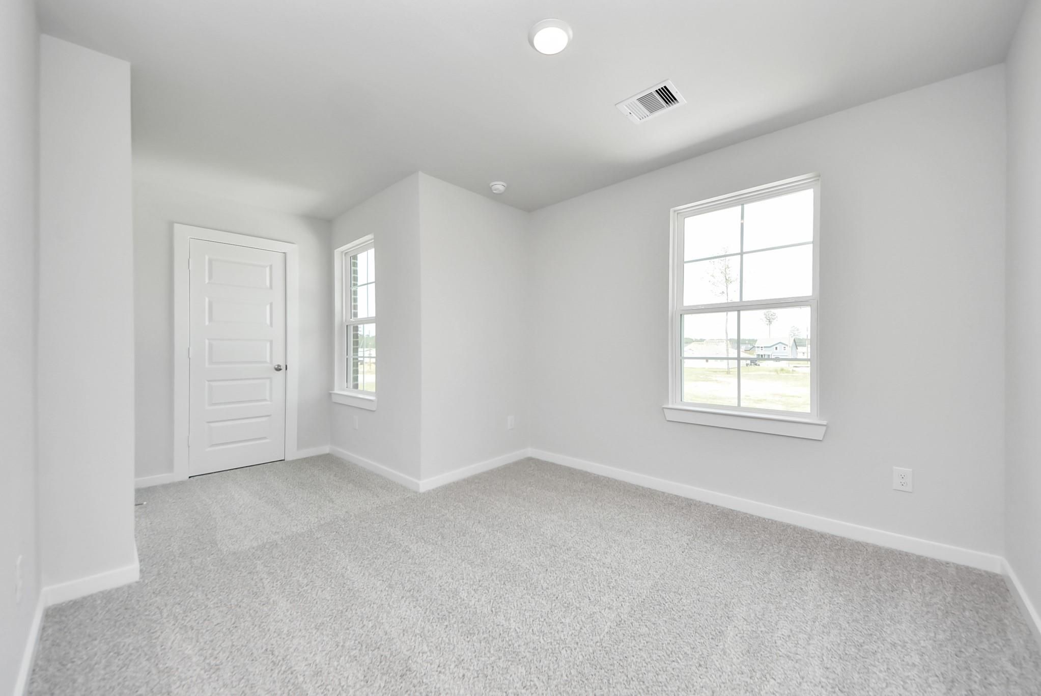 Bright, carpeted bedroom with white walls and dual windows in The Blanco F floor plan at Spring Branch Crossing, Conroe.