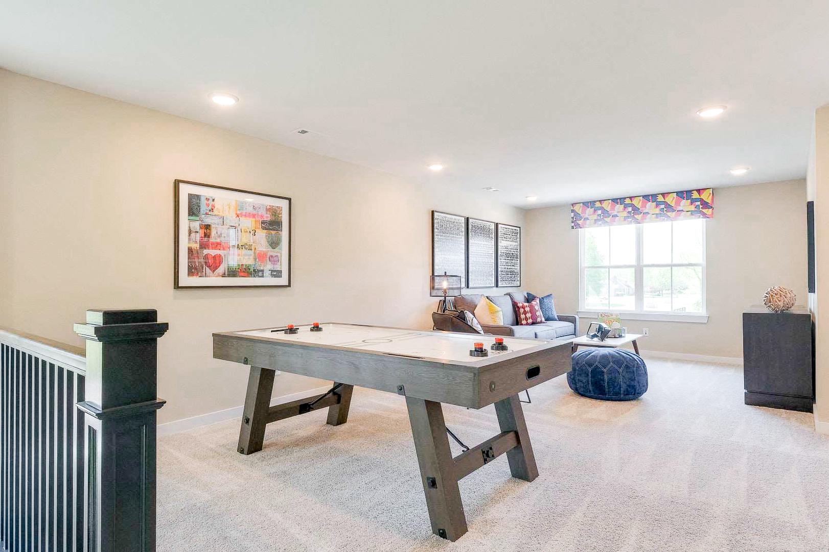 Spacious loft game room at The Meadows in Smyrna TN with gray pool table, plush couch, colorful pillows, and wood accent wall