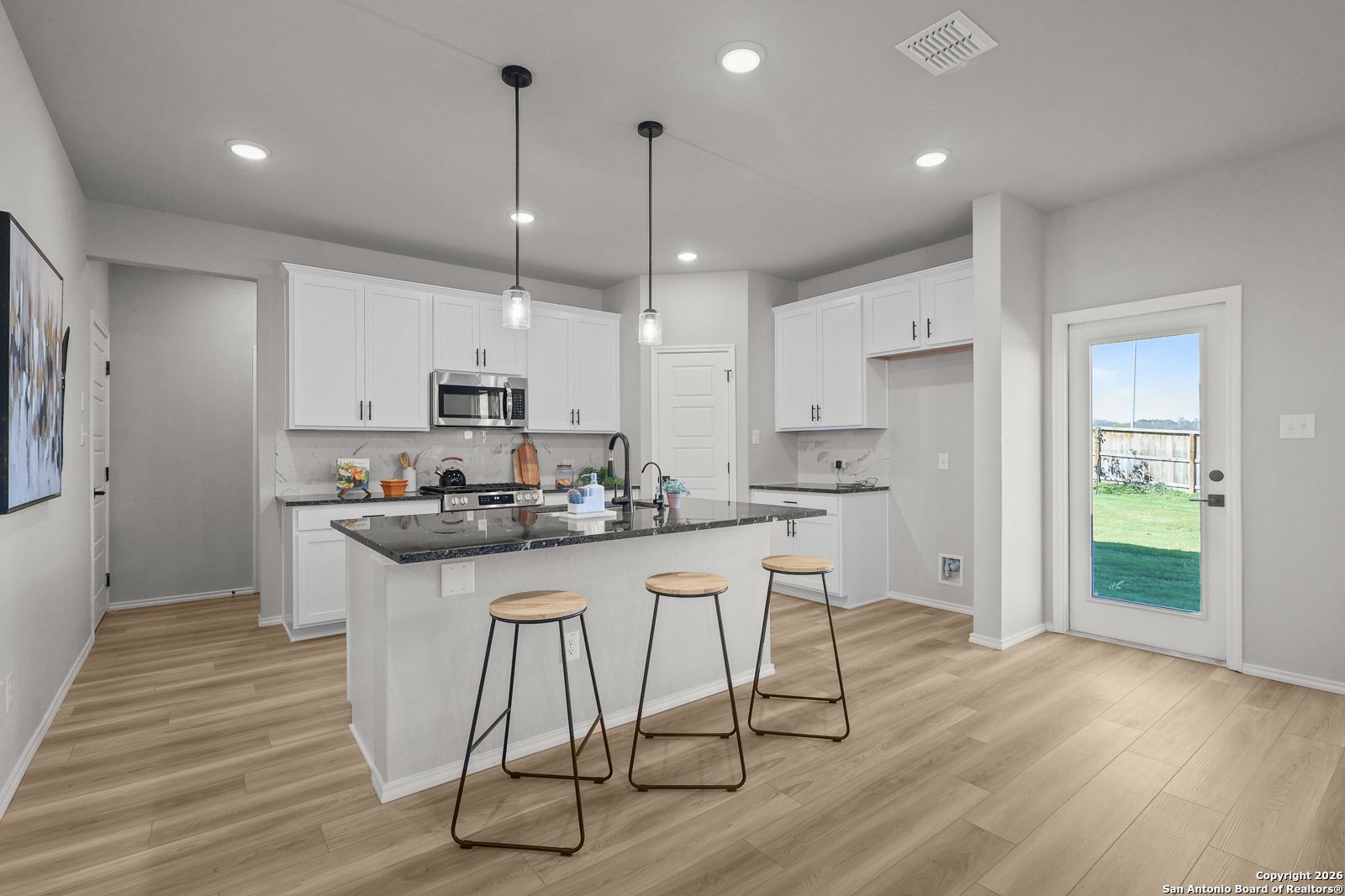 Modern open-concept kitchen with granite island, white cabinets, stainless appliances, and bar stools in Davidson Homes The Murray K, San Antonio