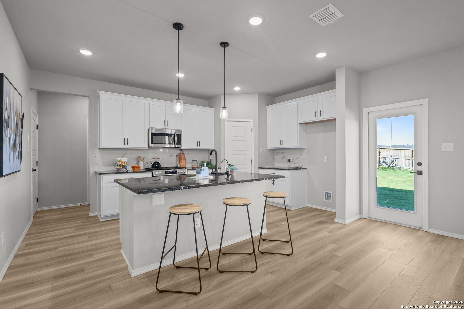 Modern open-concept kitchen with granite island, white cabinets, stainless appliances, and bar stools in Davidson Homes The Murray K, San Antonio
