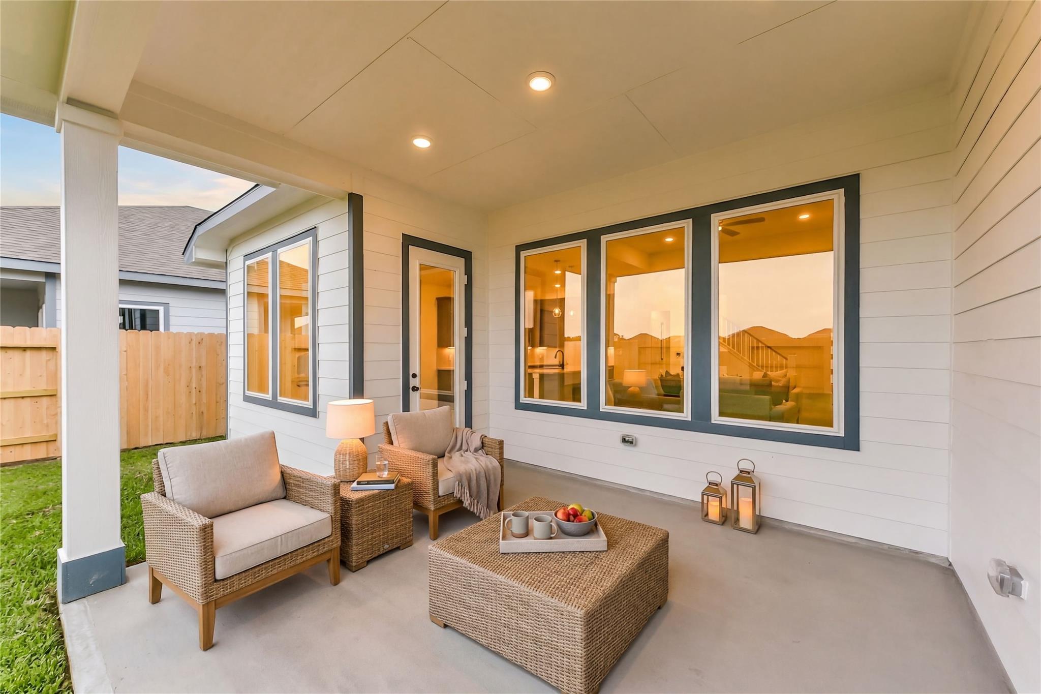 Inviting covered patio with wicker chairs, coffee table, lanterns, and large windows in Davidson Homes Sequoia C, Sundance Cove, Crosby Texas