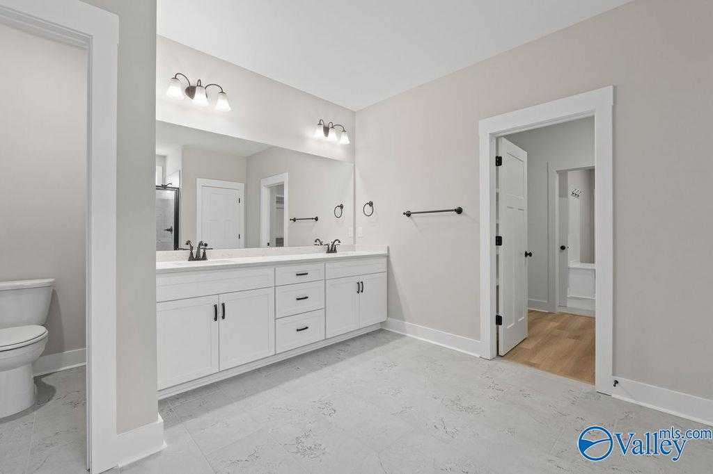 Modern master bathroom with double vanity, white cabinets, mirrors, and sconce lights in Evermore Homes The Oxford, Owens Cross Roads, Alabama