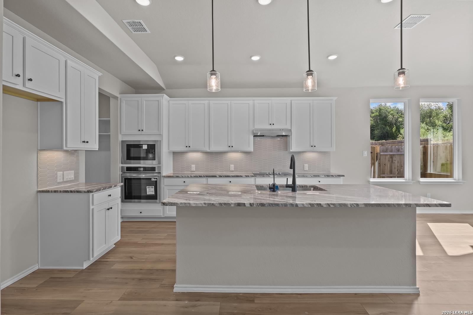 Modern kitchen with large island, white shaker cabinets, granite countertops, and pendant lights in Davidson Homes Sequoia C, San Antonio
