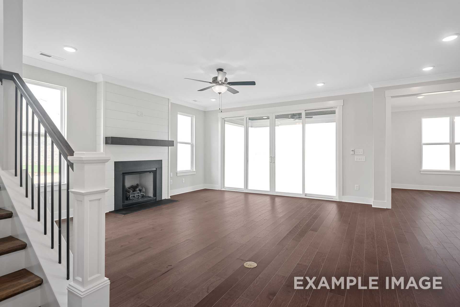 Spacious open-concept living room in The Hathaway with gas fireplace, ceiling fan, hardwood floors, and sliding glass doors
