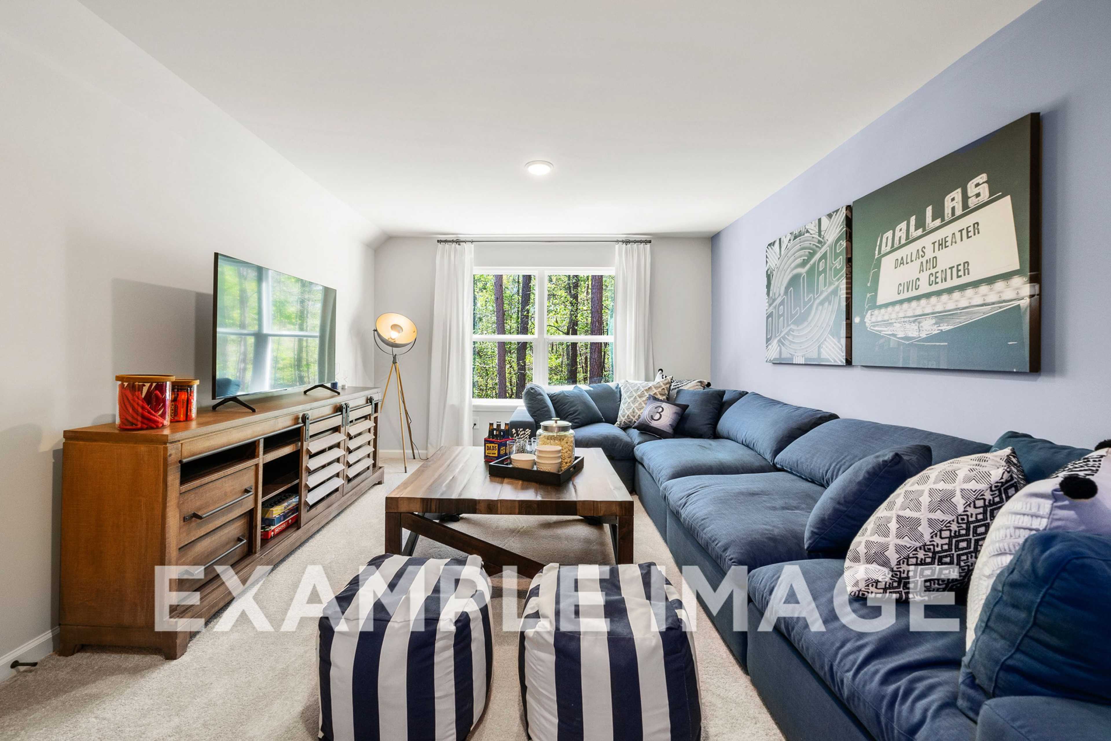 Spacious living room in The Hickory A with blue L-shaped sectional sofa, wooden coffee table, media console, and large windows