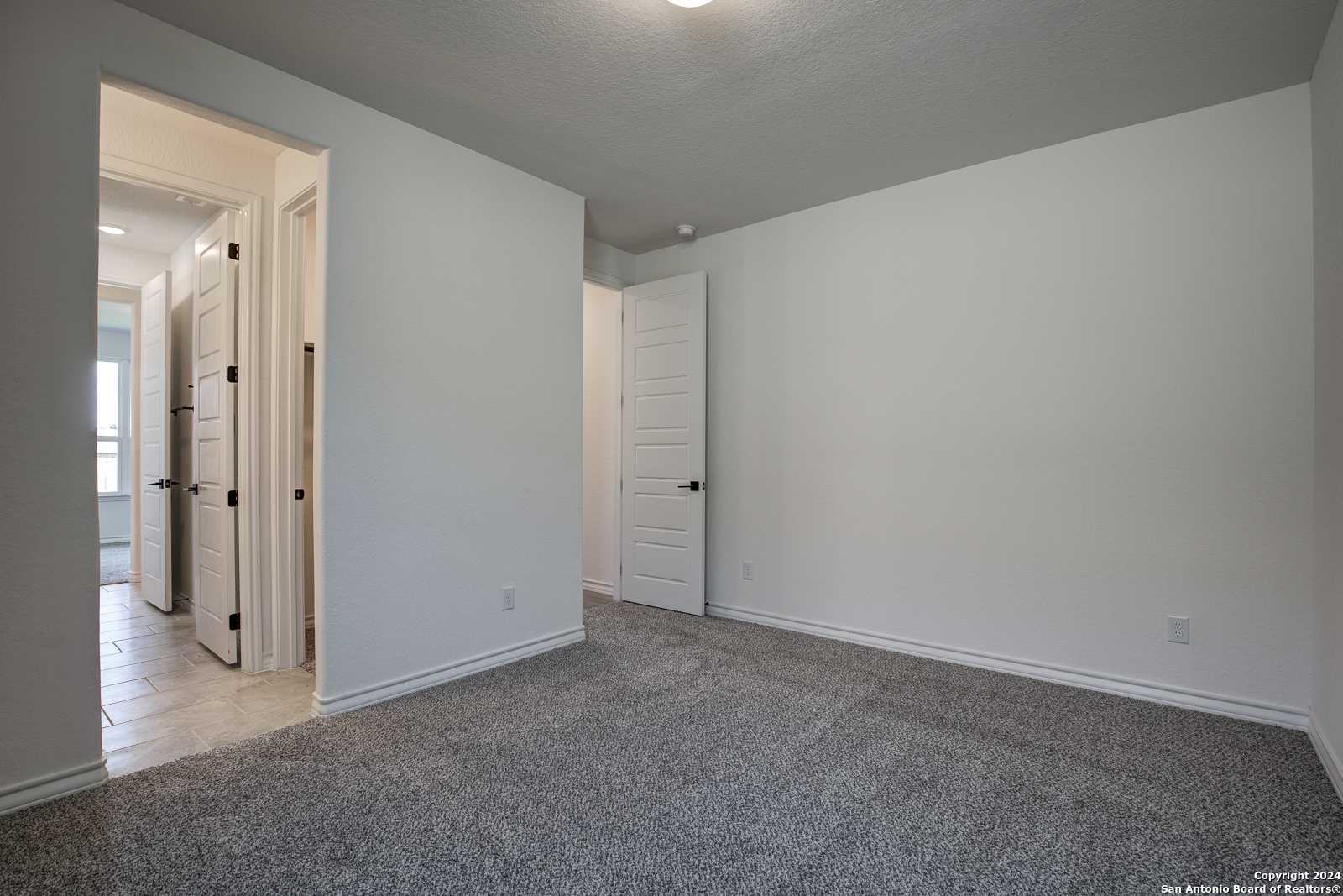 Spacious secondary bedrooms with gray carpet, white doors, and open hallway in Davidson Homes The Garner B, Castroville, Texas