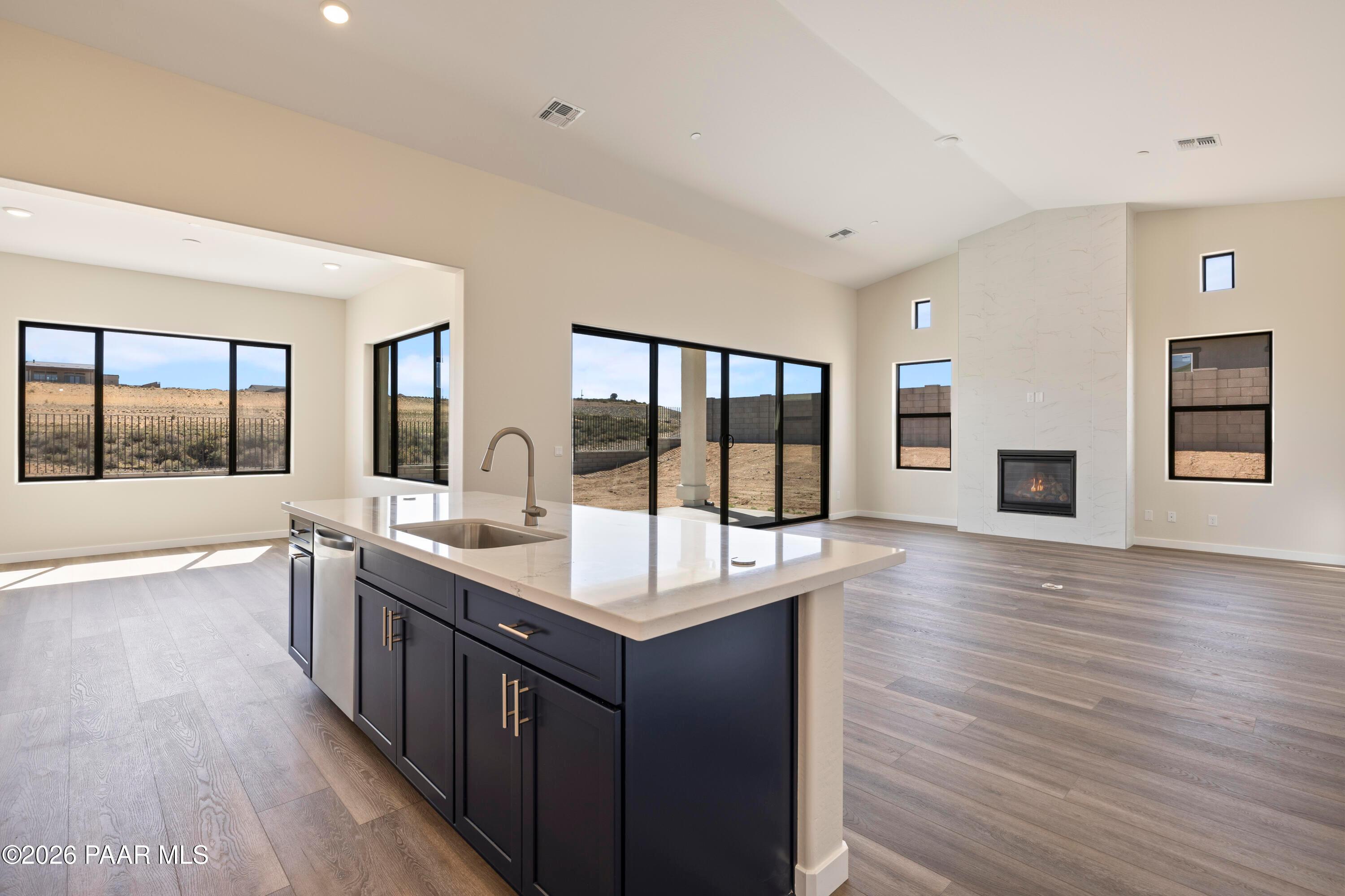 Open kitchen with white quartz island, navy cabinets, stainless sink, and gas fireplace in The Soleil E, Hidden Hills, Prescott, Arizona