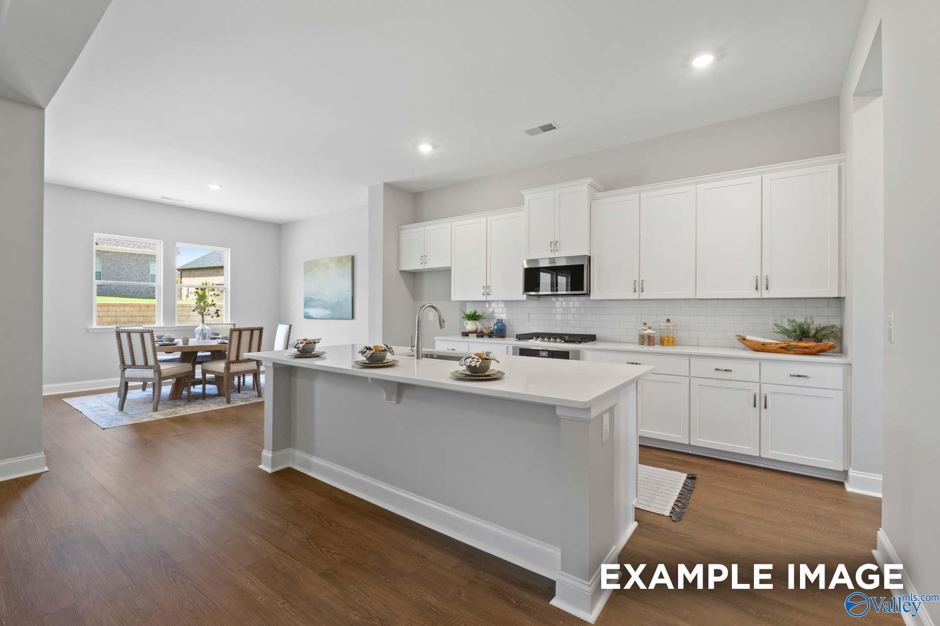 Modern open-concept kitchen featuring white shaker cabinets, quartz island, stainless appliances, and adjacent dining nook in Evermore Homes The Haven E, Owens Cross Roads, Alabama