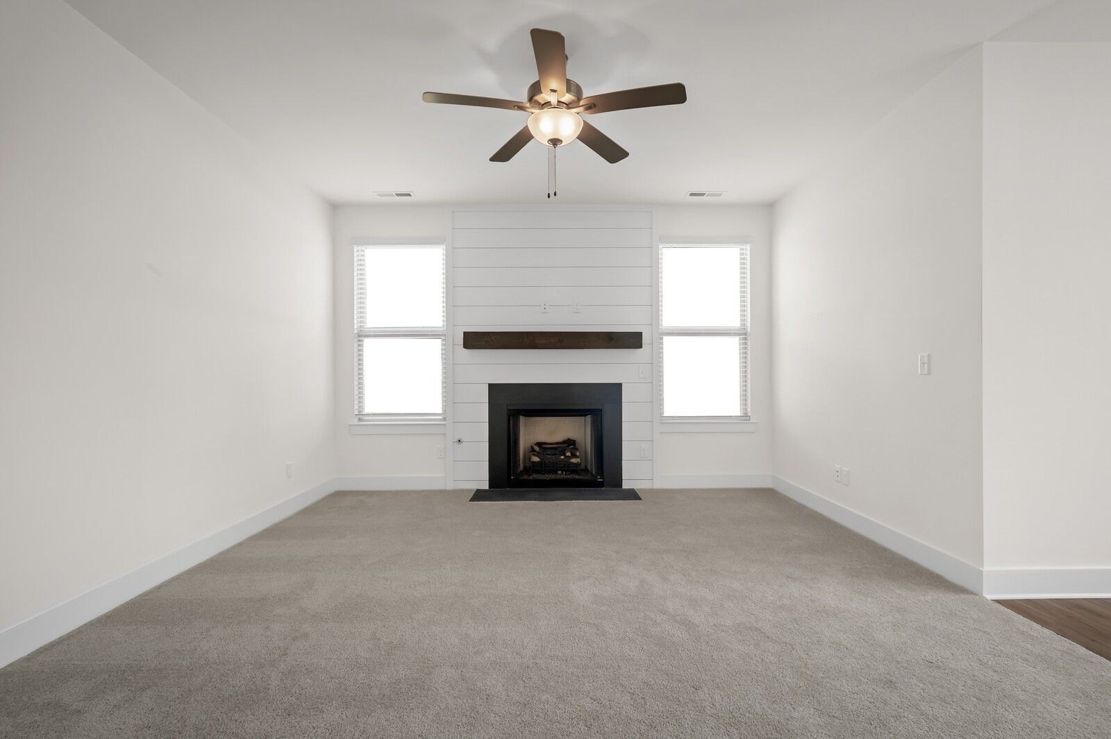 Living room with shiplap fireplace, ceiling fan, and carpet in The Ash A floor plan at Woods Crossing in Gallatin, TN.