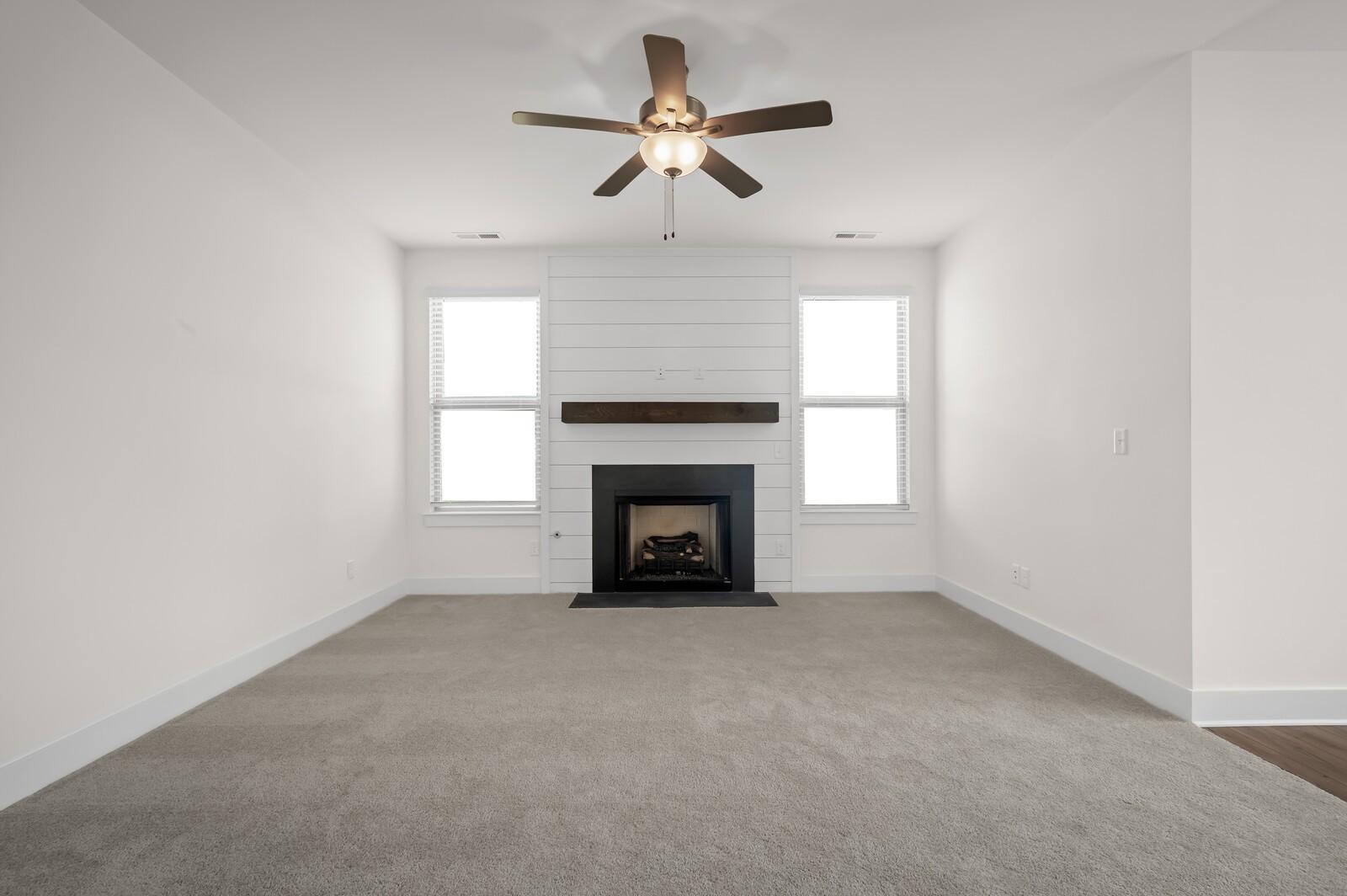 Living room with shiplap fireplace, ceiling fan, and carpet in The Ash A floor plan at Woods Crossing in Gallatin, TN.