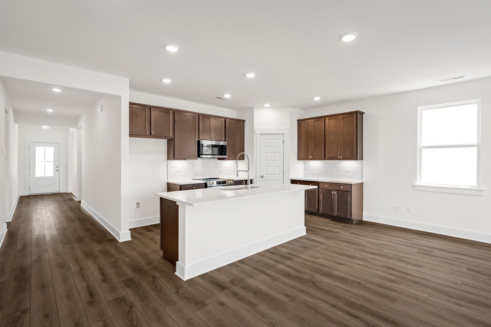Open-concept kitchen with white island, dark wood cabinets, and luxury vinyl plank flooring in Davidson Homes Cottonwood E, Gallatin TN