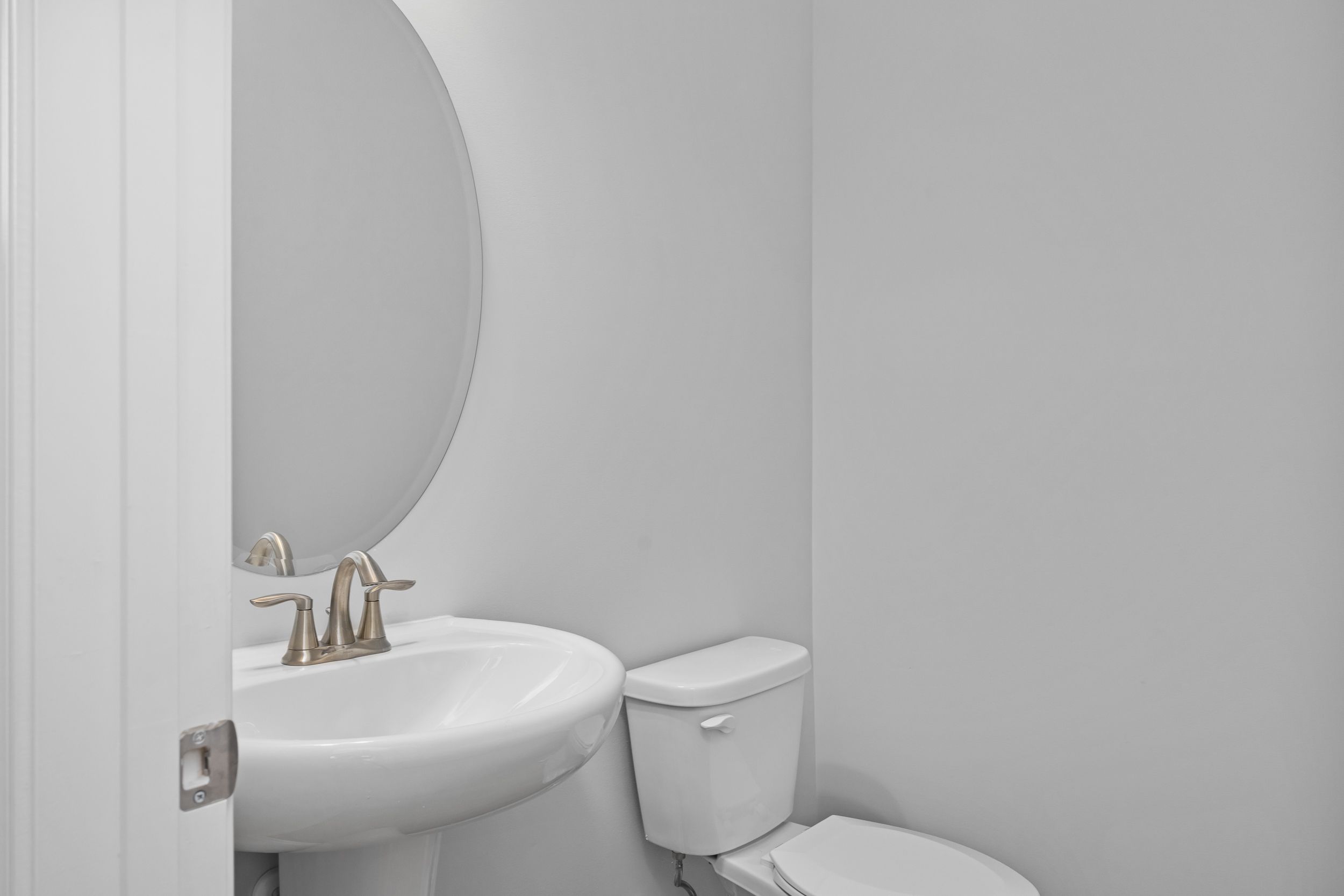 Modern powder room in The Durham featuring a white pedestal sink, brushed nickel faucet, and oval mirror.