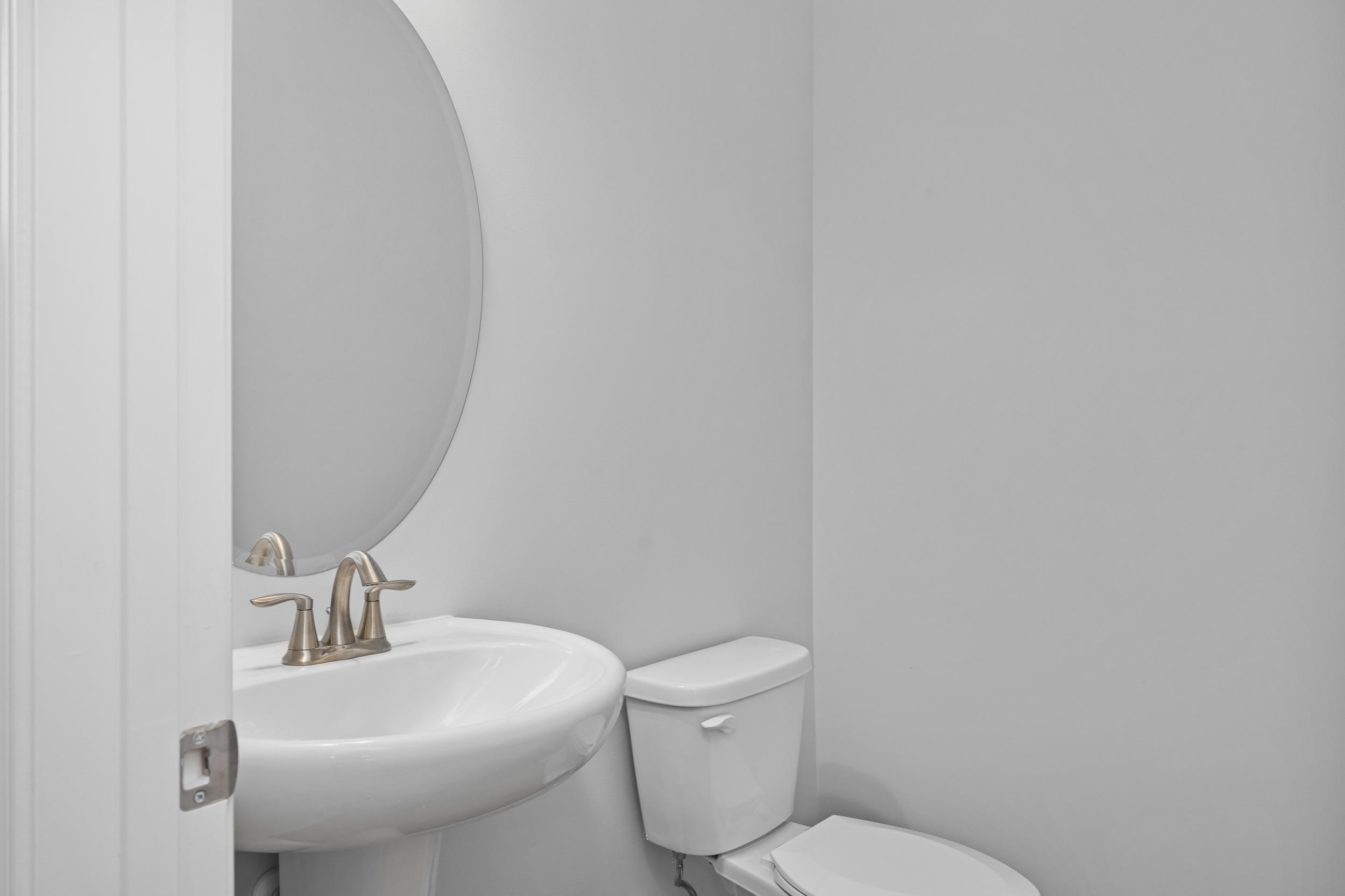 Modern powder room in The Durham featuring a white pedestal sink, brushed nickel faucet, and oval mirror.