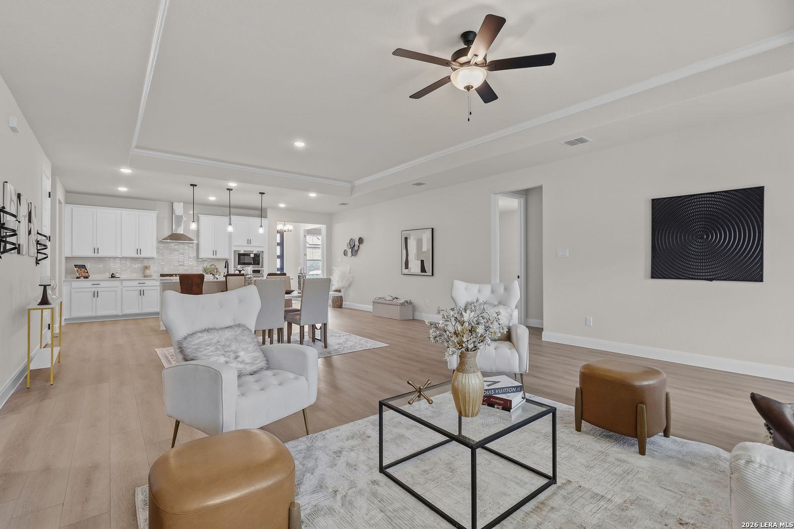 Open-concept living and dining space with white armchairs, modern kitchen, ceiling fan, and hardwood floors in The Lanier G, Castroville, Texas