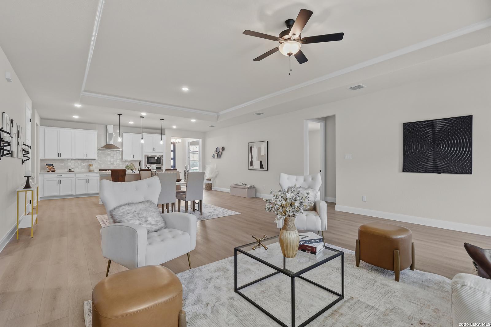 Open-concept living and dining space with white armchairs, modern kitchen, ceiling fan, and hardwood floors in The Lanier G, Castroville, Texas