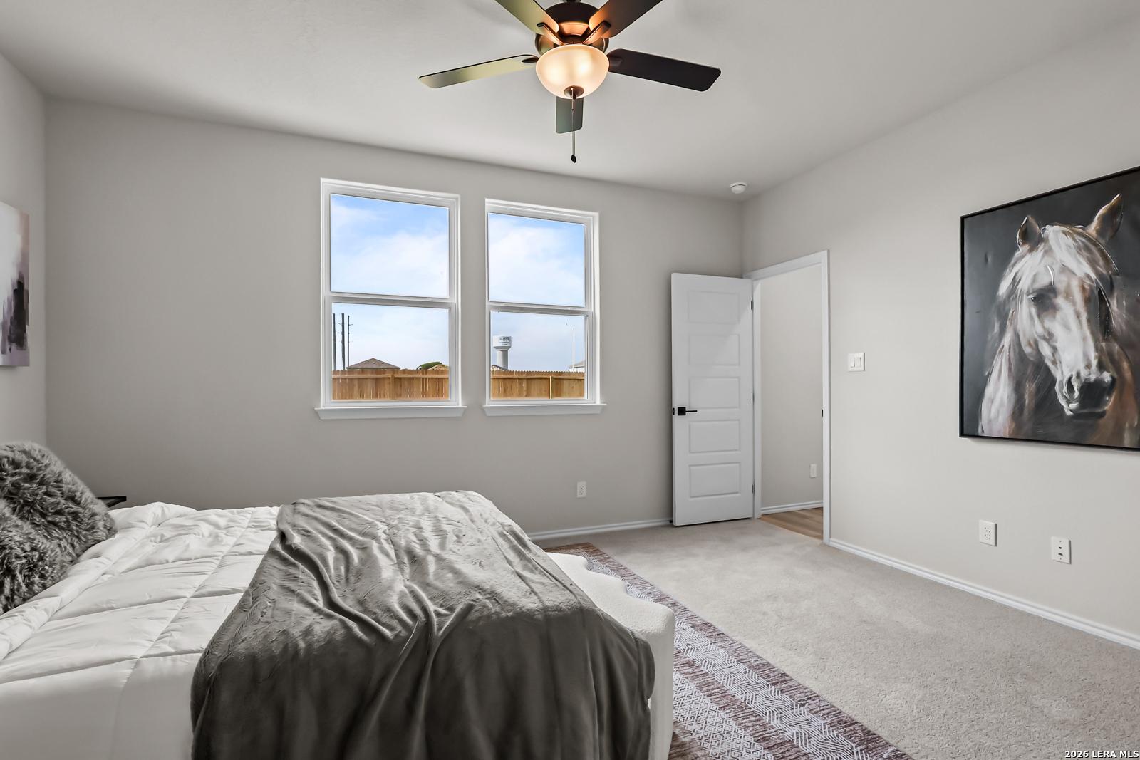 Spacious bedroom with neutral decor, ceiling fan, and large windows in The Douglas C floor plan at Hannah Heights, Seguin.