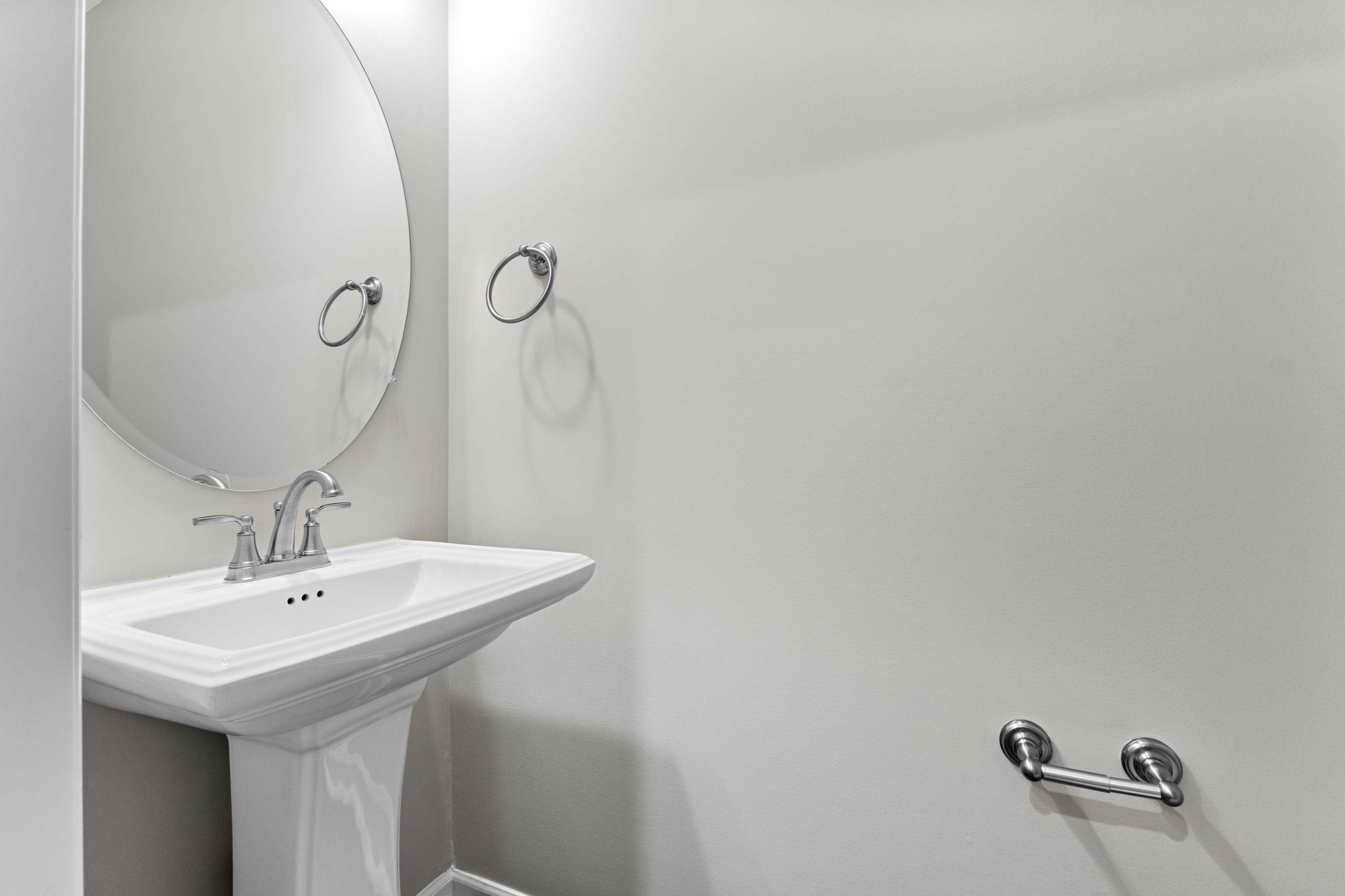 Modern powder room in The Haven E by Evermore Homes featuring white pedestal sink, round mirror, and chrome fixtures