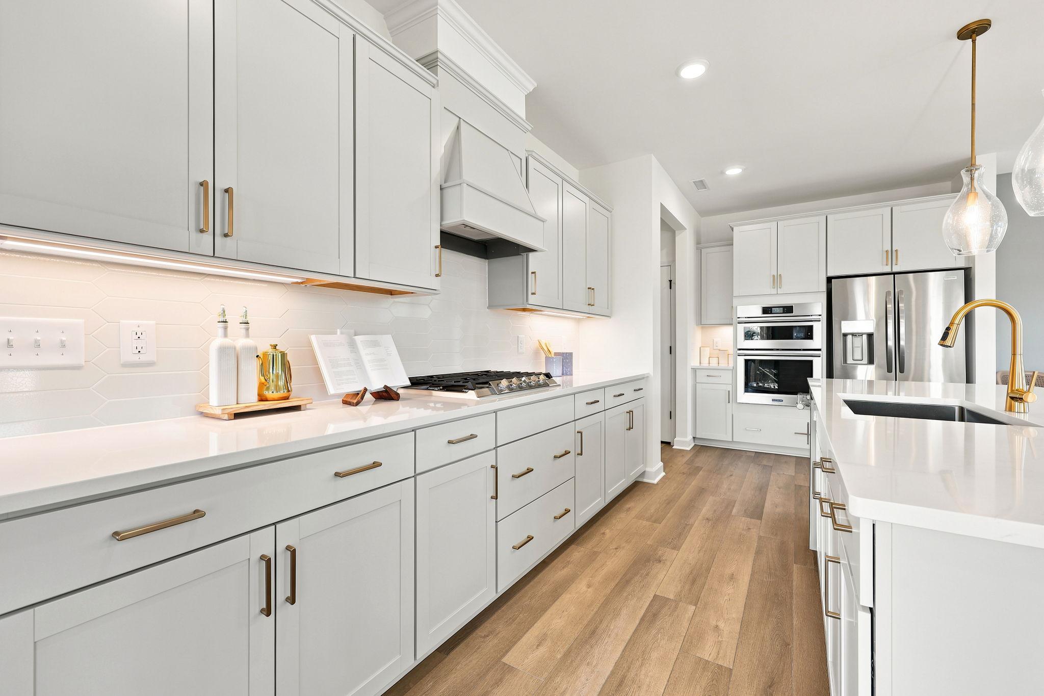 Modern kitchen at Montrose in Aberdeen, NC by Davidson Homes featuring white cabinets, quartz countertops, and gold accents.