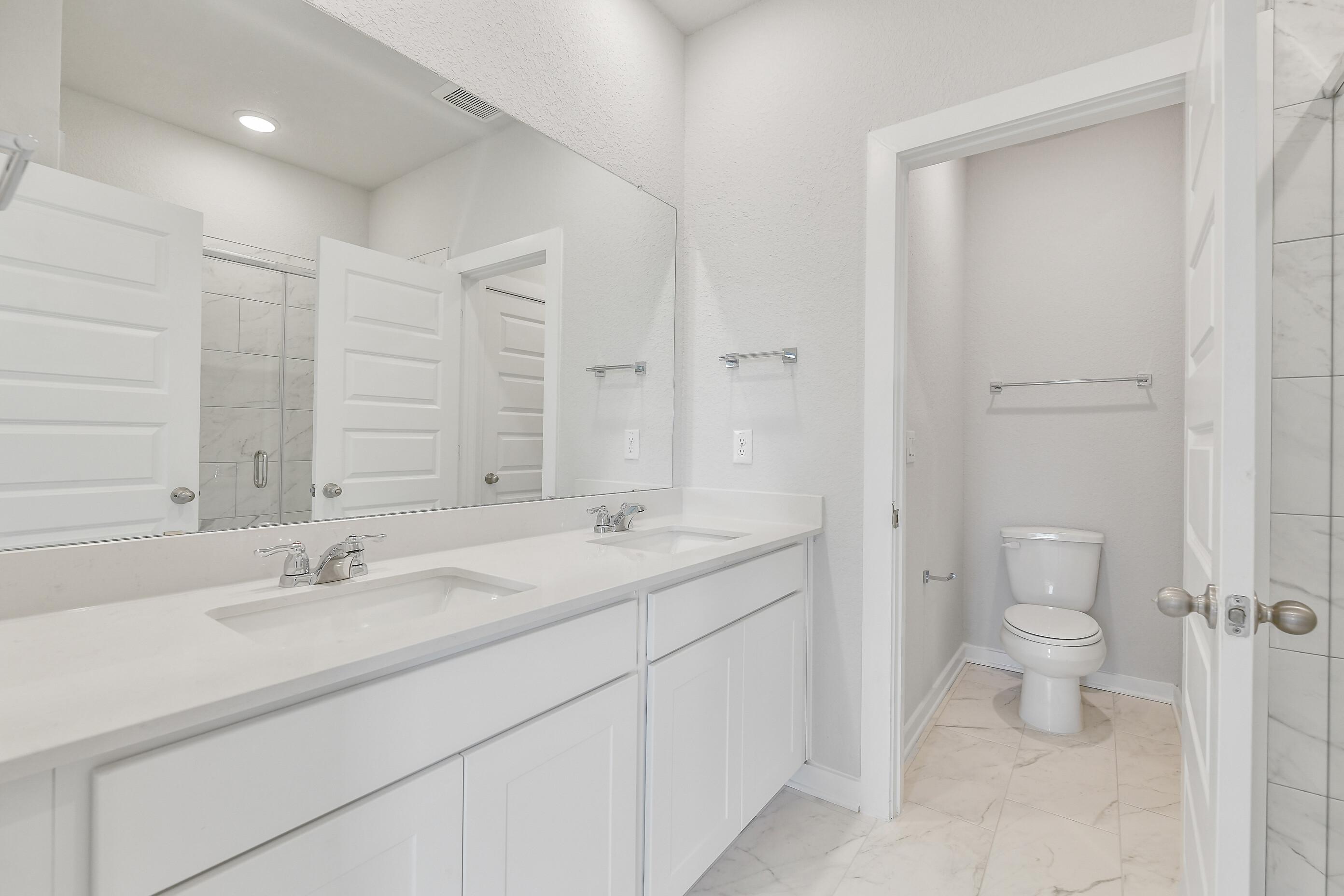 Modern double vanity bathroom with white quartz counters, mirrors, and subway tile shower in Davidson Homes The Colorado G, Magnolia Texas