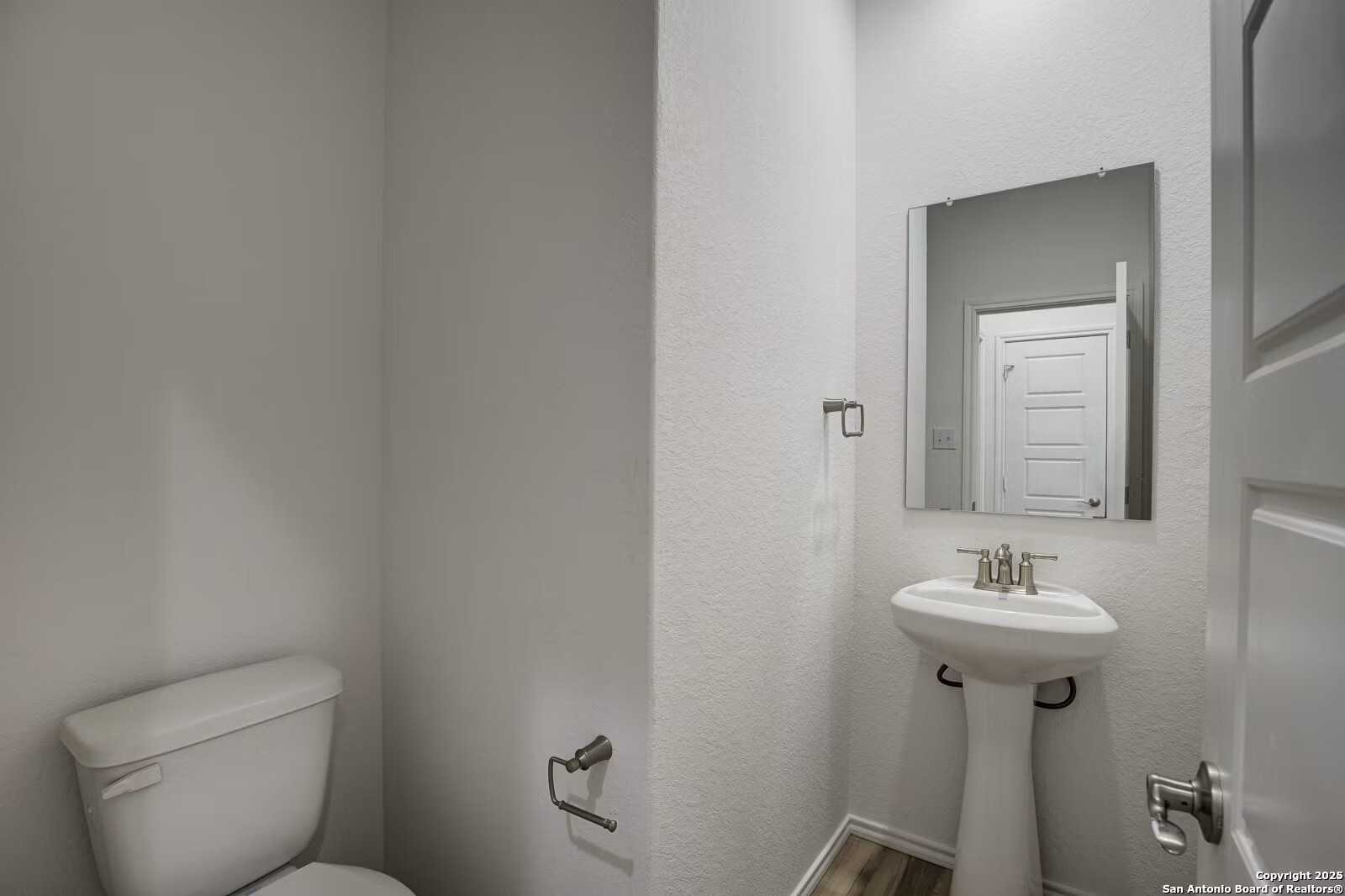 Modern powder room with pedestal sink, toilet, frameless mirror in Davidson Homes The Douglas B, Seguin, Texas
