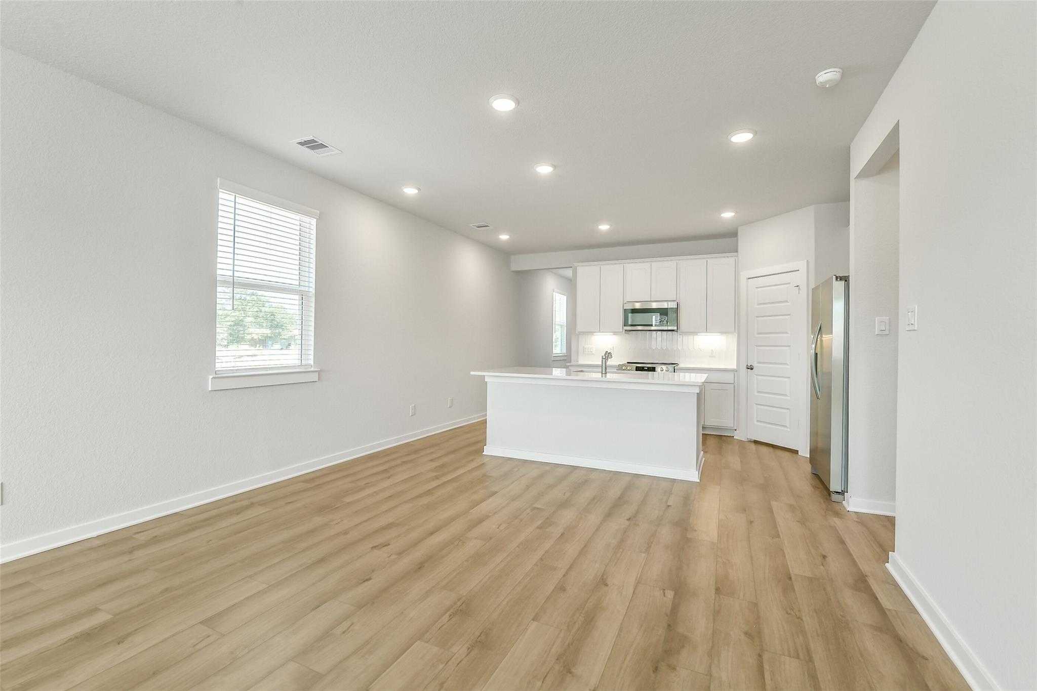 Modern open kitchen with white island, stainless appliances, recessed lighting, and light wood floors in The San Marcos E home, Cleveland TX