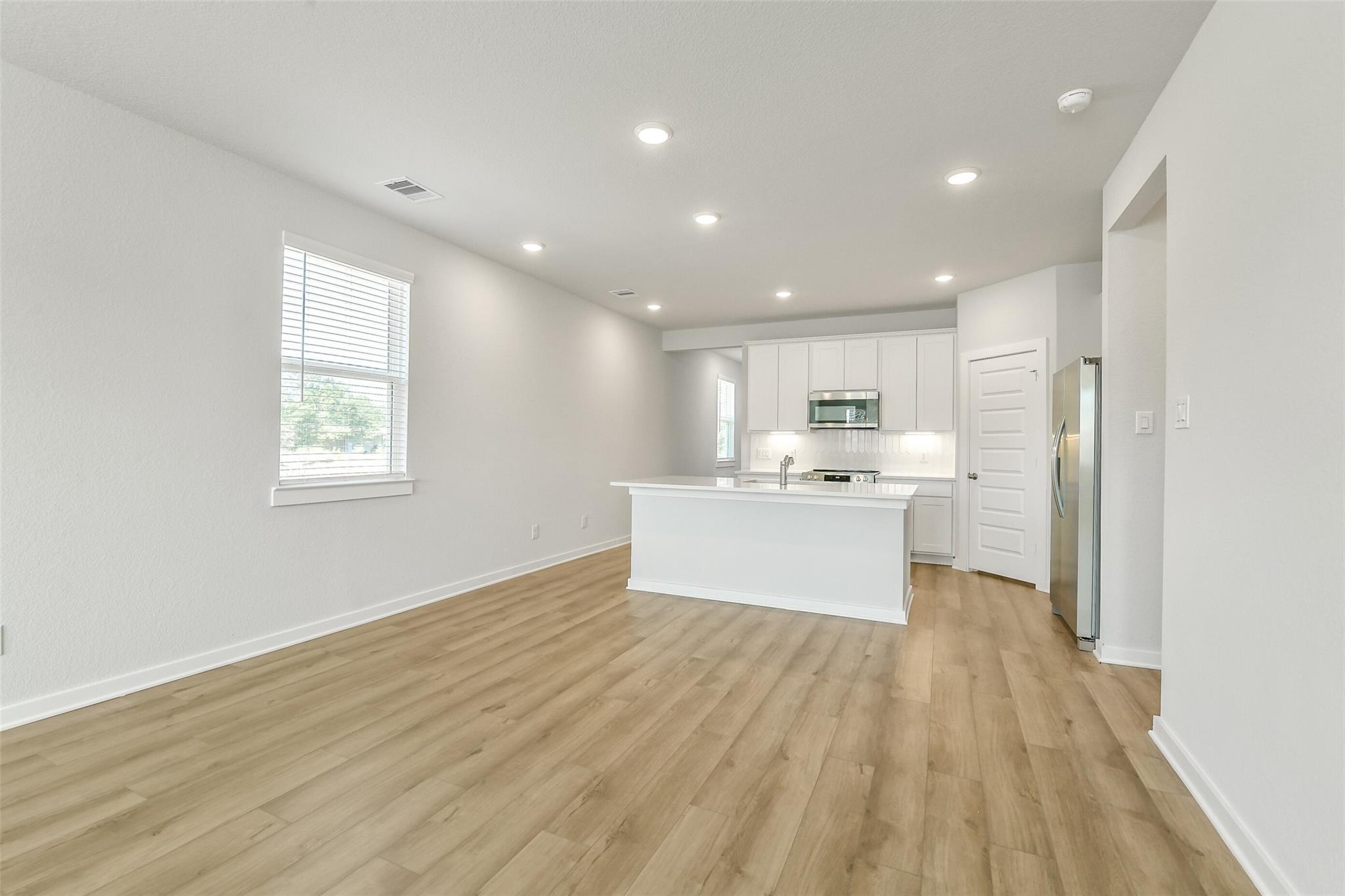 Modern open kitchen with white island, stainless appliances, recessed lighting, and light wood floors in The San Marcos E home, Cleveland TX