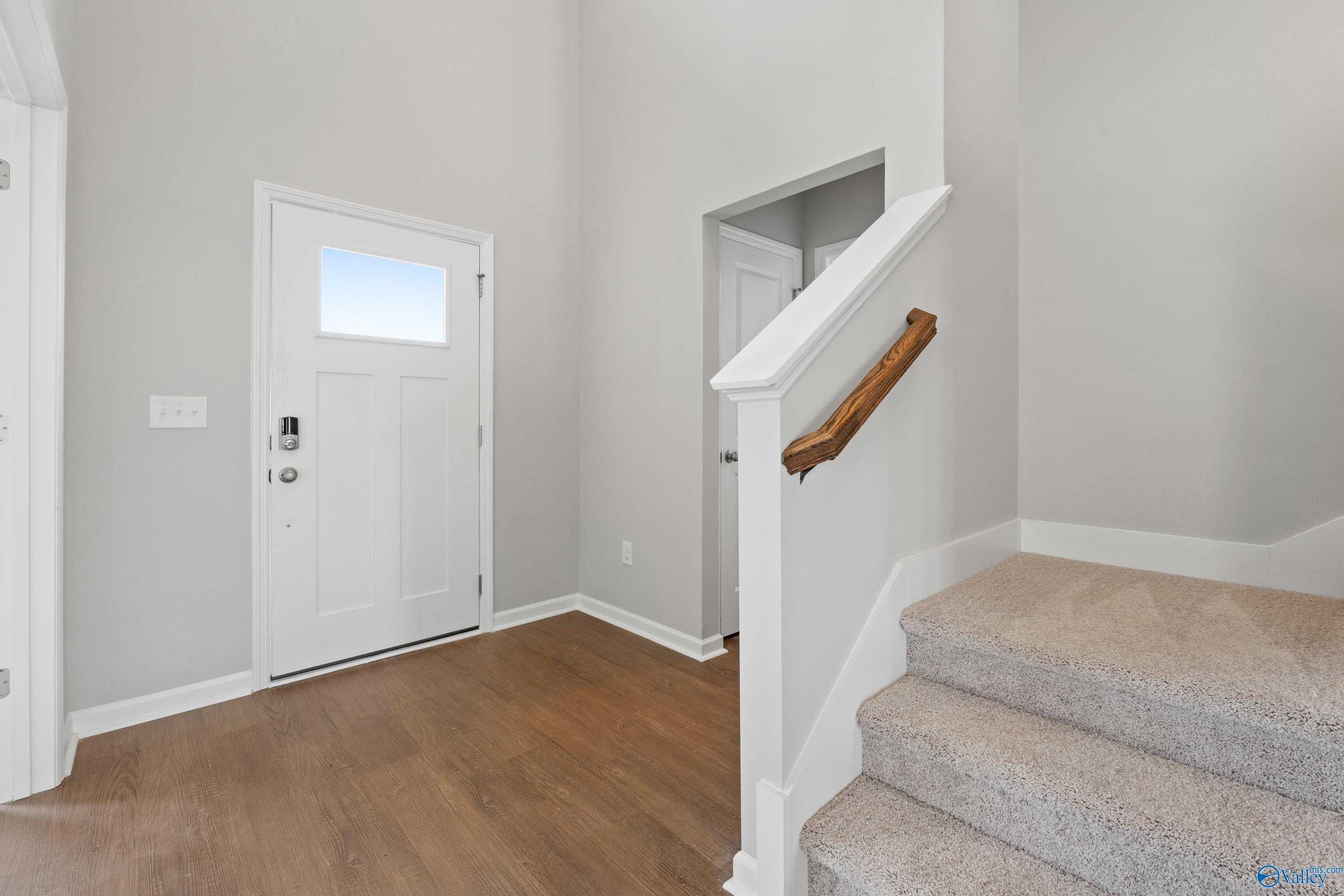 Welcoming foyer with light wood flooring, white front door, and carpeted staircase in Davidson Homes The Dorado, Athens, Alabama