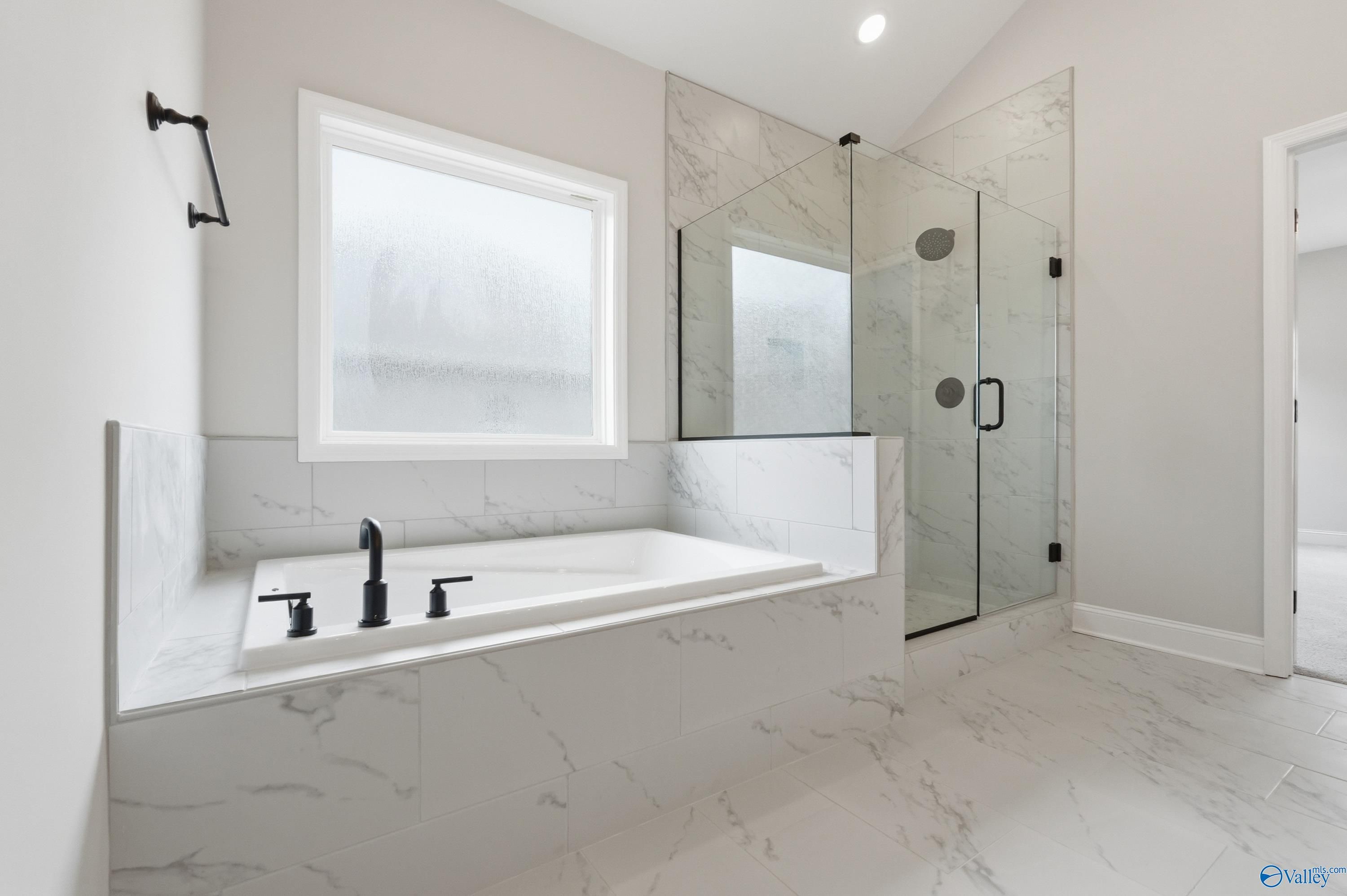 Modern master bathroom with freestanding tub, glass shower, white marble tiles in Davidson Homes The Finleigh, Meridianville, Alabama