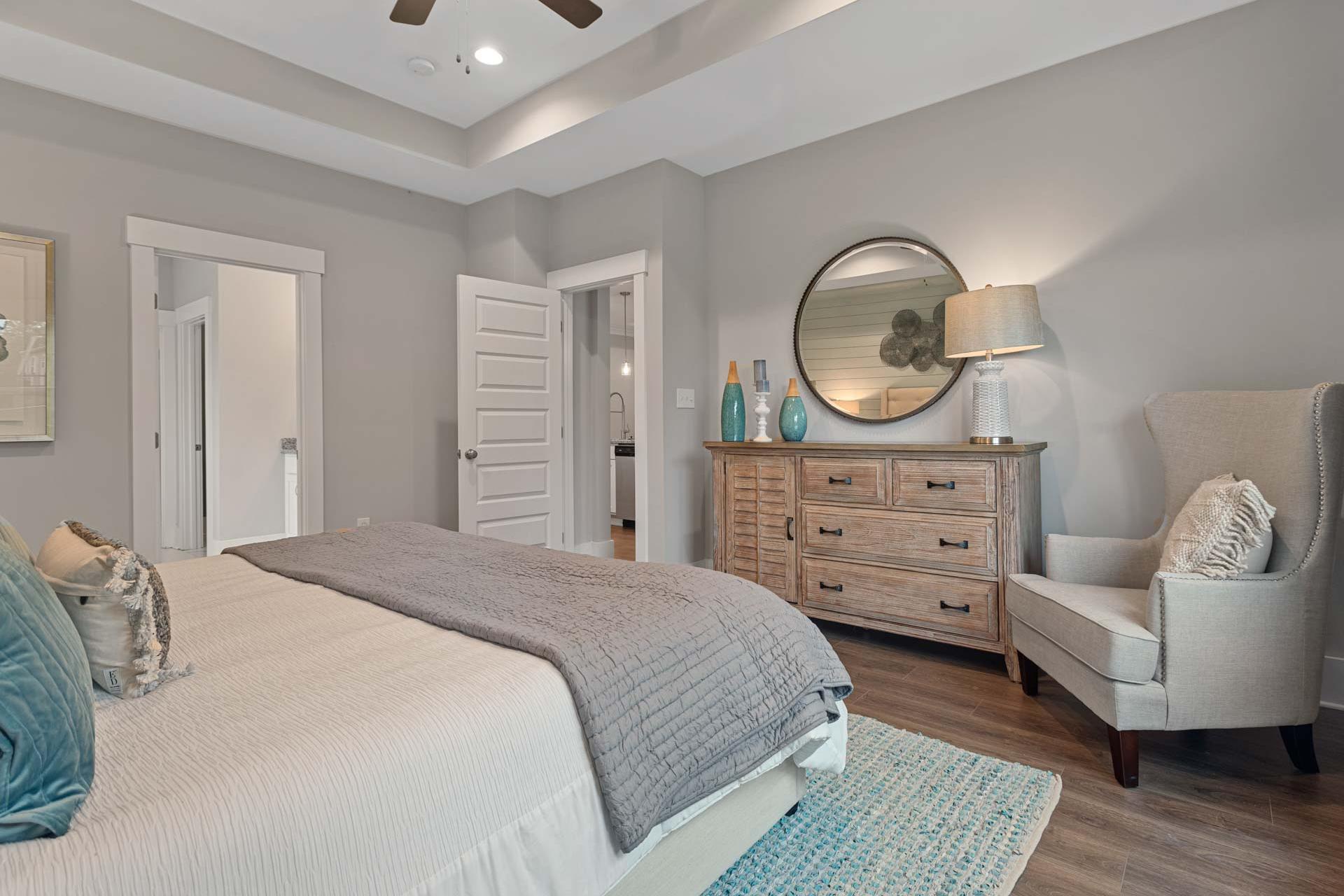 Spacious master bedroom at Monteagle Cove in Owens Cross Roads AL with gray walls, king bed, wooden dresser, round mirror, and armchair