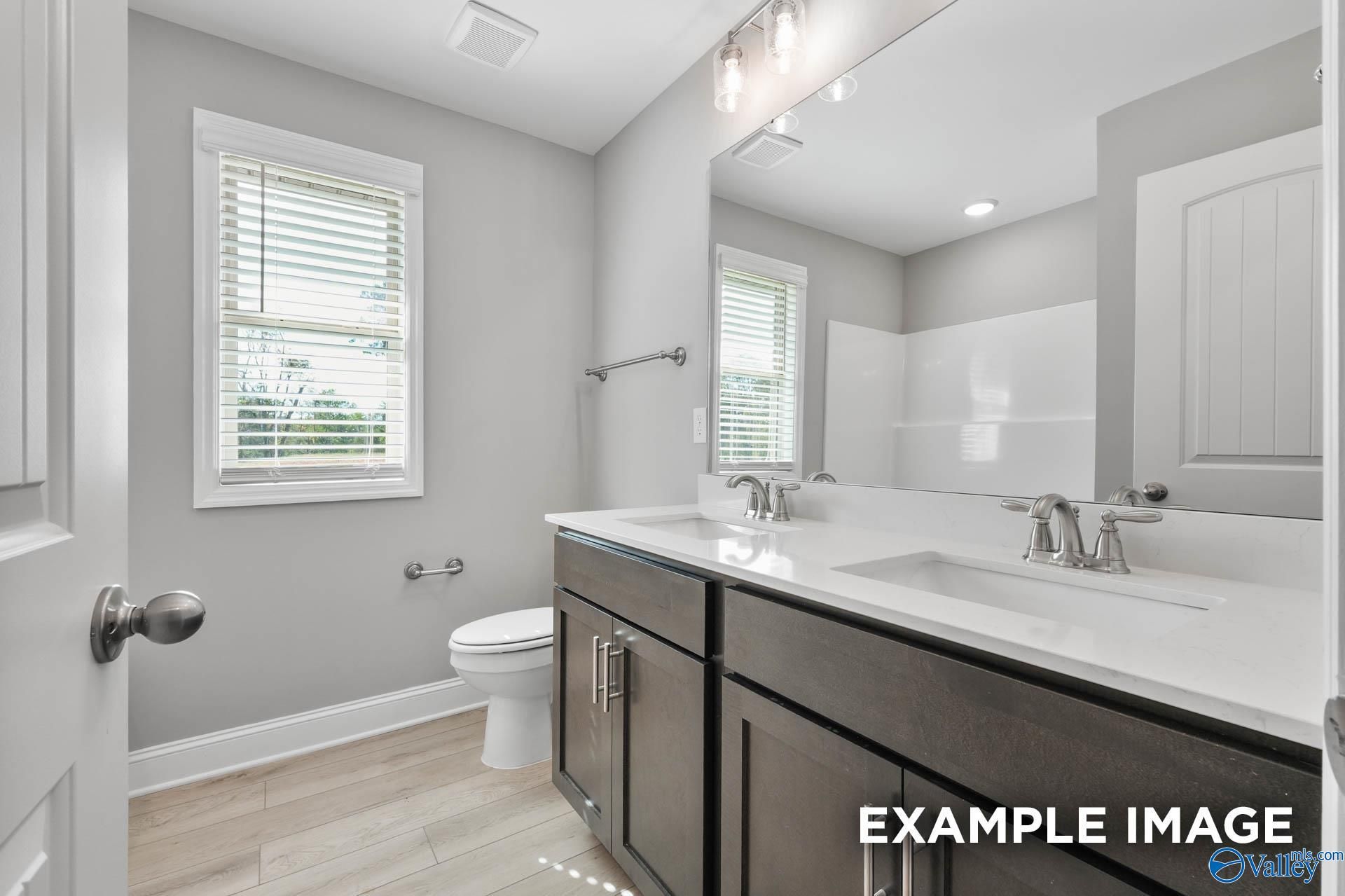 Modern double vanity bathroom with white quartz counters, dark cabinets, and subway tile shower in Davidson Homes The Everett B, Toney, Alabama