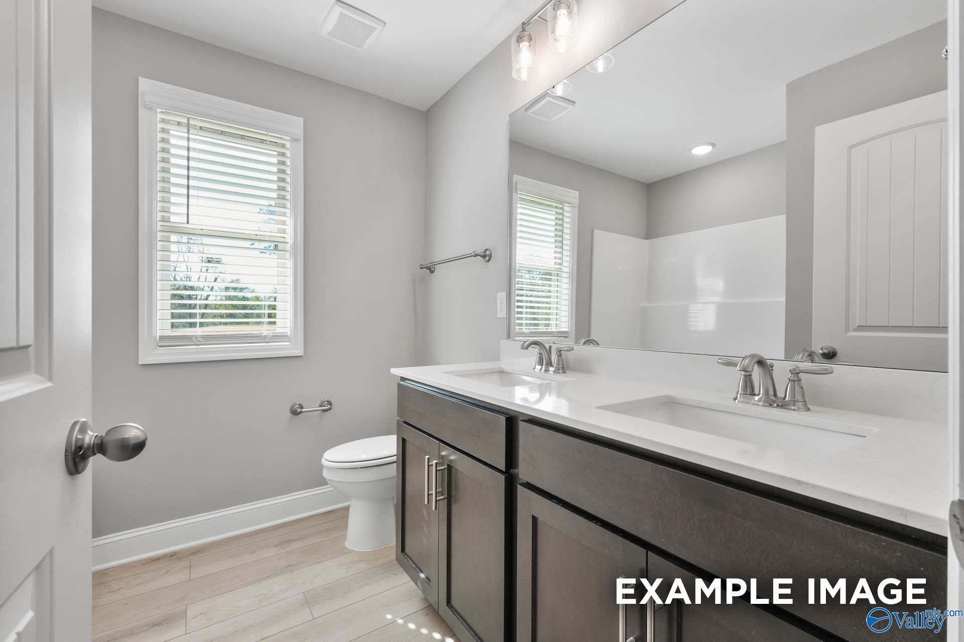Modern double vanity bathroom with white quartz counters, dark cabinets, and subway tile shower in Davidson Homes The Everett B, Toney, Alabama