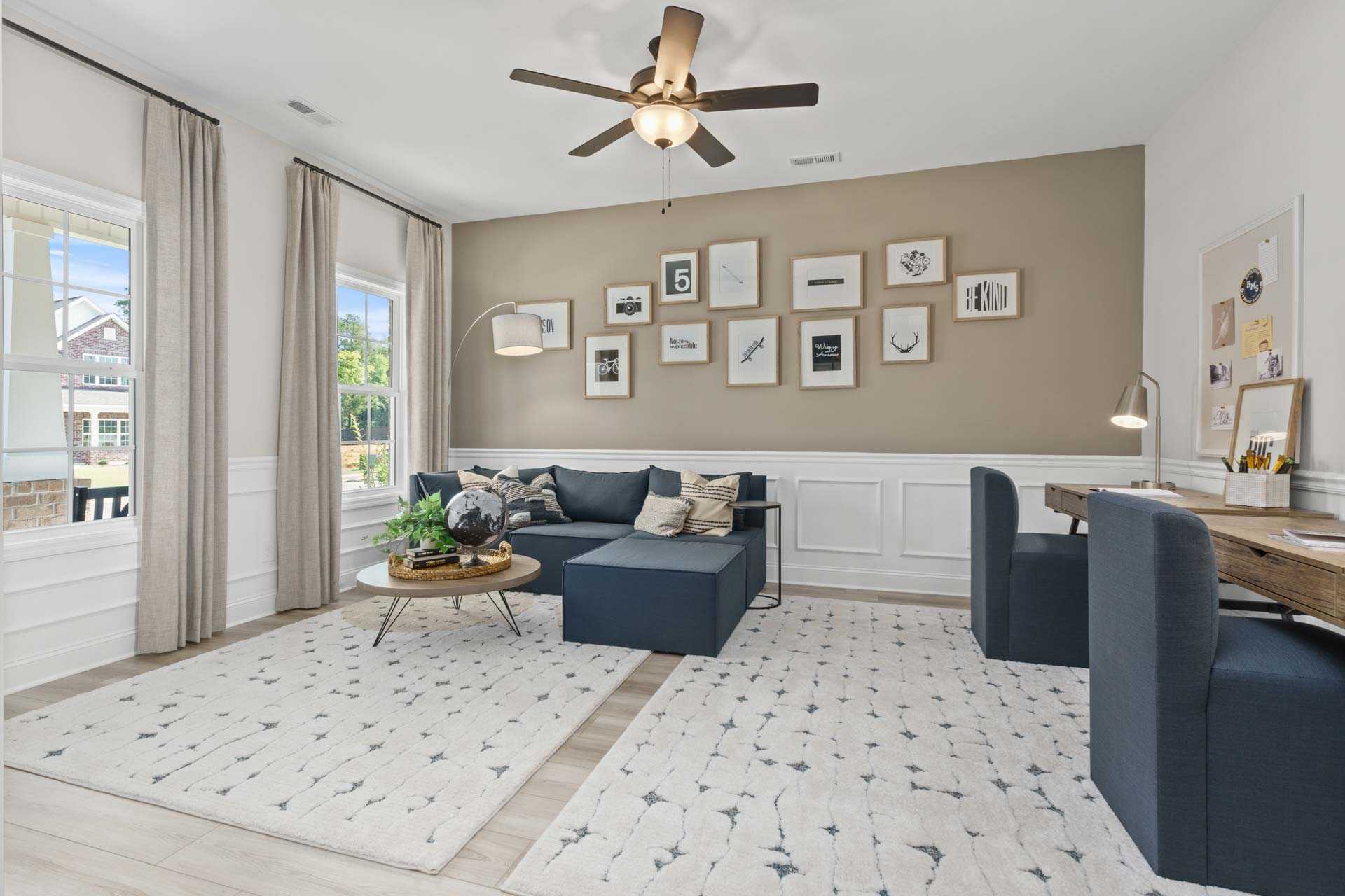 Cozy den in Creek Grove New Market Alabama by Davidson Homes featuring blue sectional sofa, desk, wall art gallery, and large windows