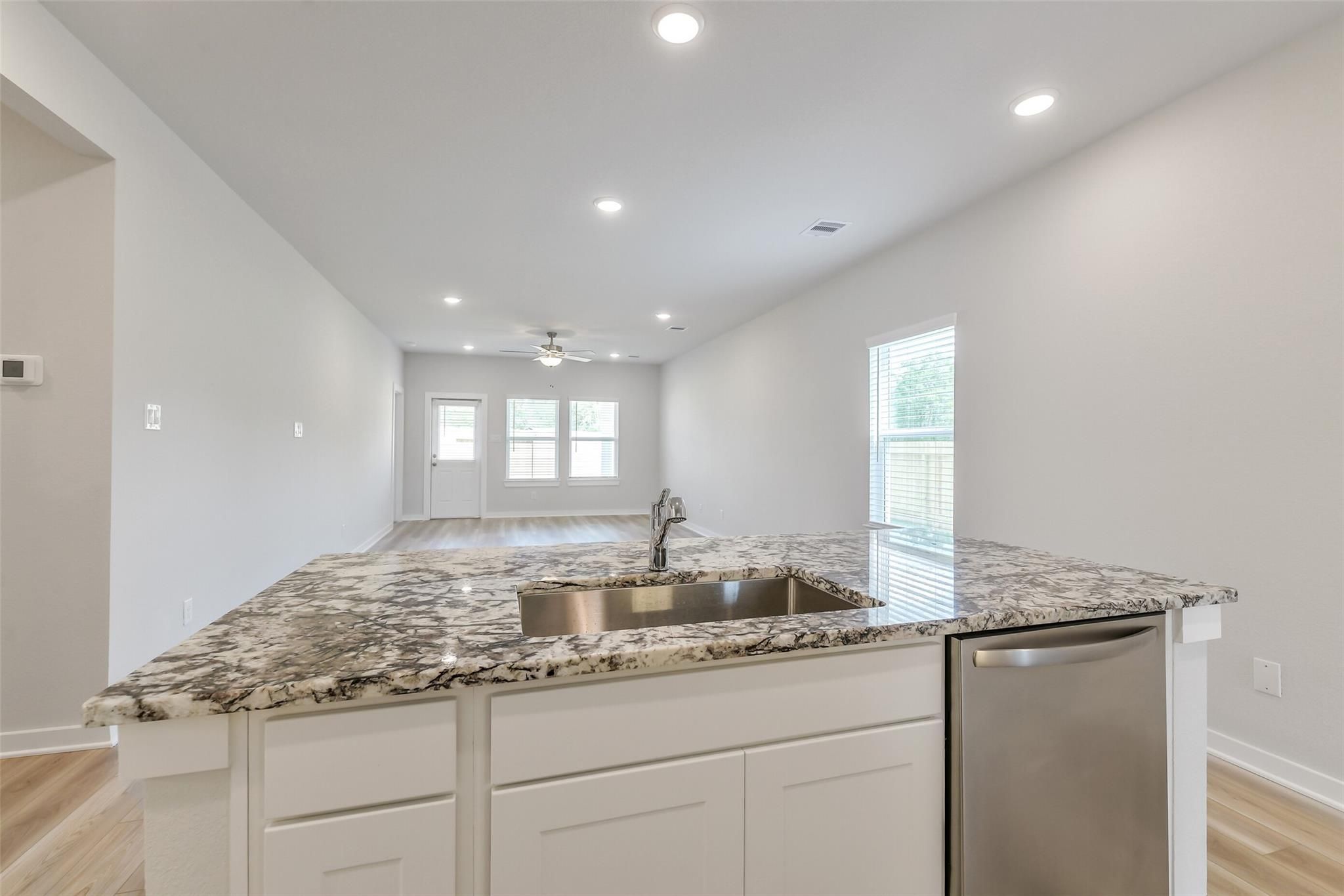 Modern kitchen island with granite countertops, stainless sink, white cabinets, open to hallway in The San Marcos E, Conroe, Texas
