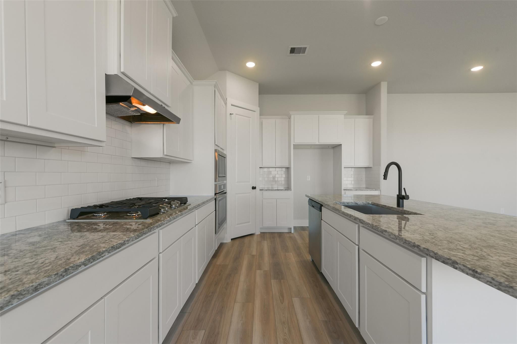 Modern white kitchen with granite island, stainless appliances, subway tile backsplash in Davidson Homes Edward C, Texas City