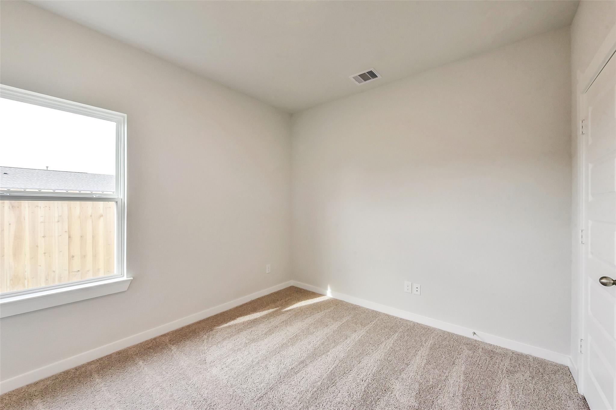 Bright secondary bedroom with beige carpet, white walls, and window overlooking fence in Davidson Homes The Frio G, Dayton, TX
