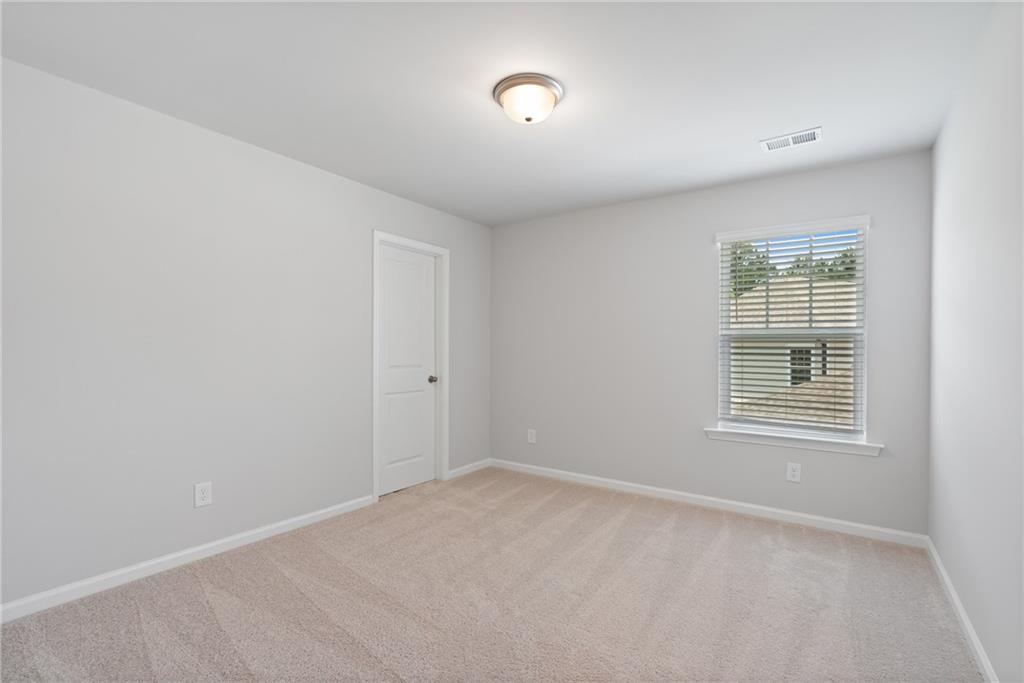 Bright secondary bedroom with light gray walls, beige carpet, window blinds, and flush door in Davidson Homes The Hickory A, Winder, Georgia