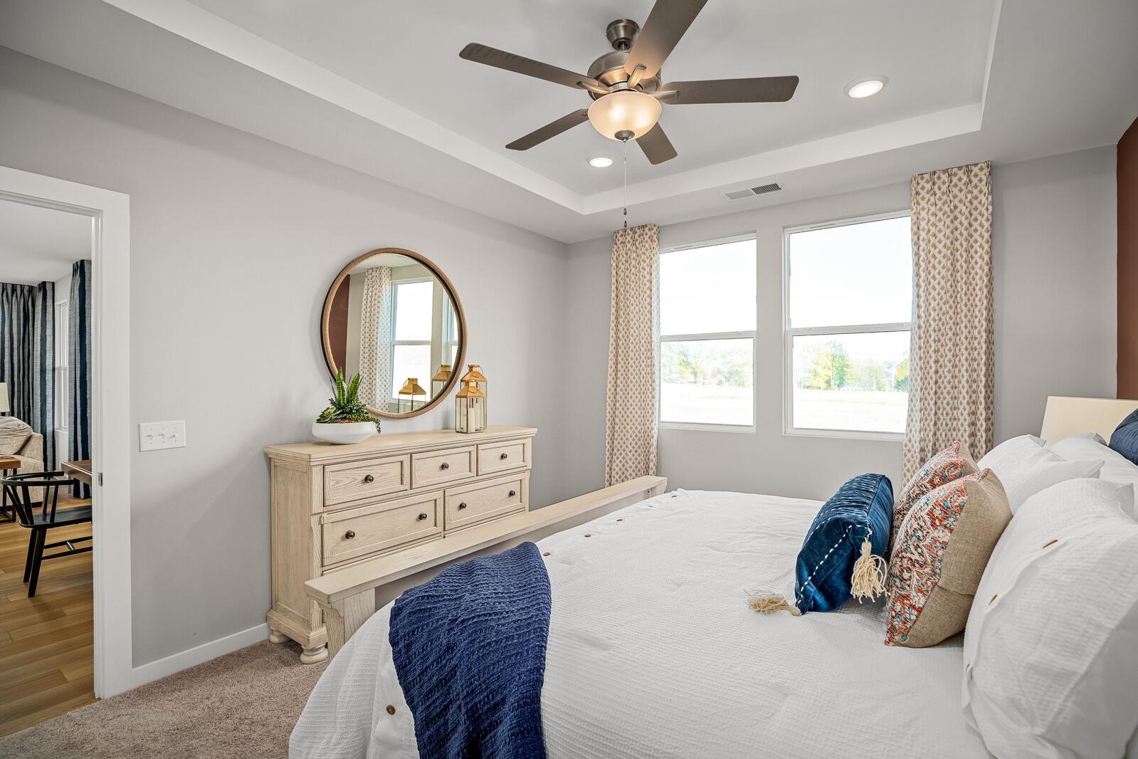 Spacious primary bedroom at Sage Farms in White House TN with gray walls, white king bed, wooden dresser, and large curtained windows