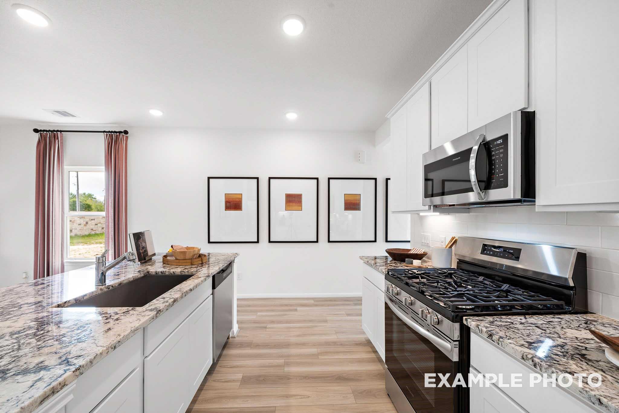 Modern kitchen with granite countertops, white cabinetry, and stainless steel appliances in The Sabine E, Liberty Estates.