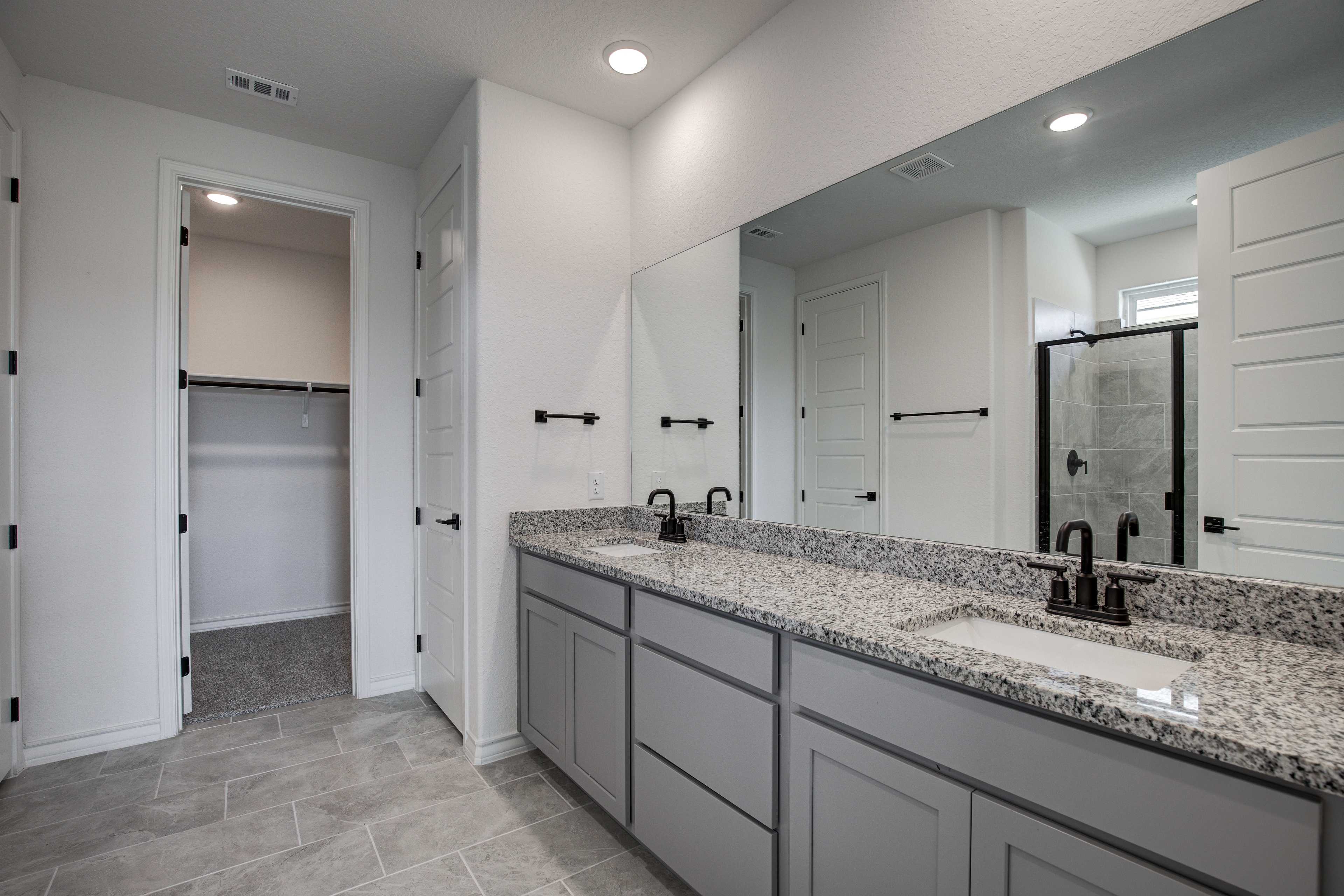 Spacious master bathroom in The Lanier with double gray vanity, granite counters, frameless shower, and walk-in closet