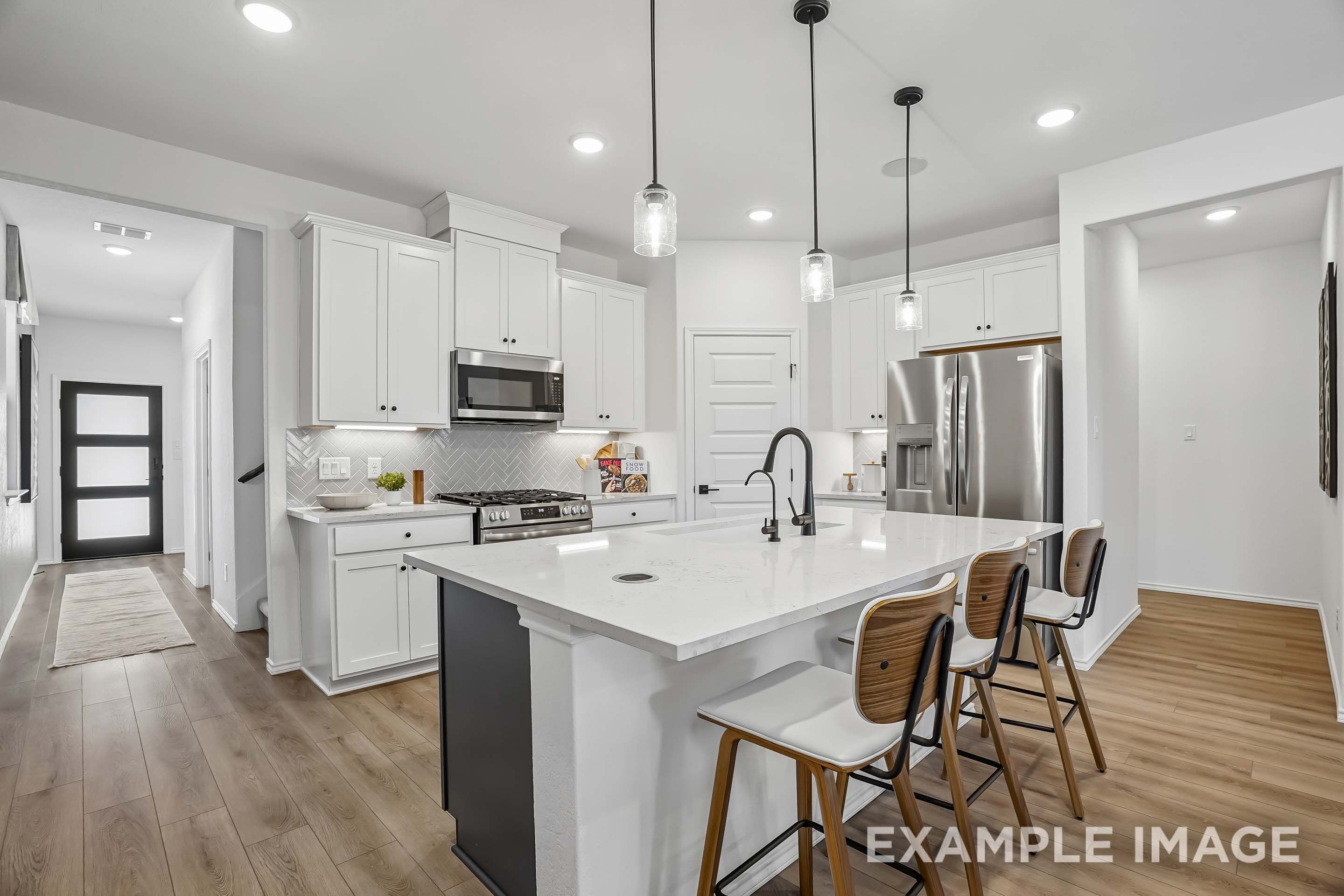 Modern kitchen in The Pinecrest D featuring white cabinetry, quartz island, stainless steel appliances, and wood flooring.